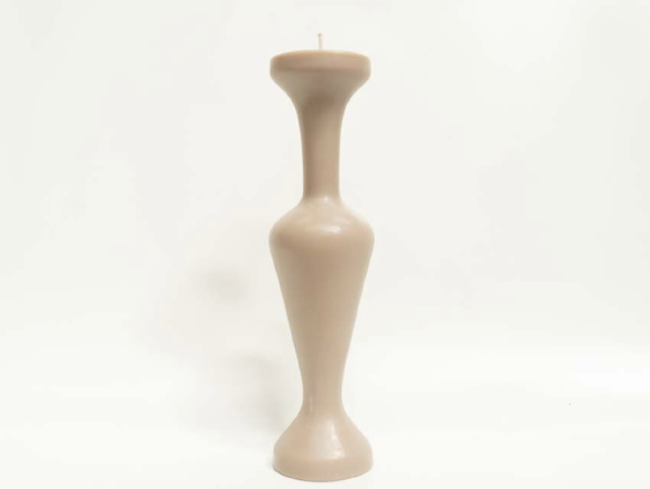 A beige tall candle with a narrow middle and flared top, standing on a flat surface against a plain white background.