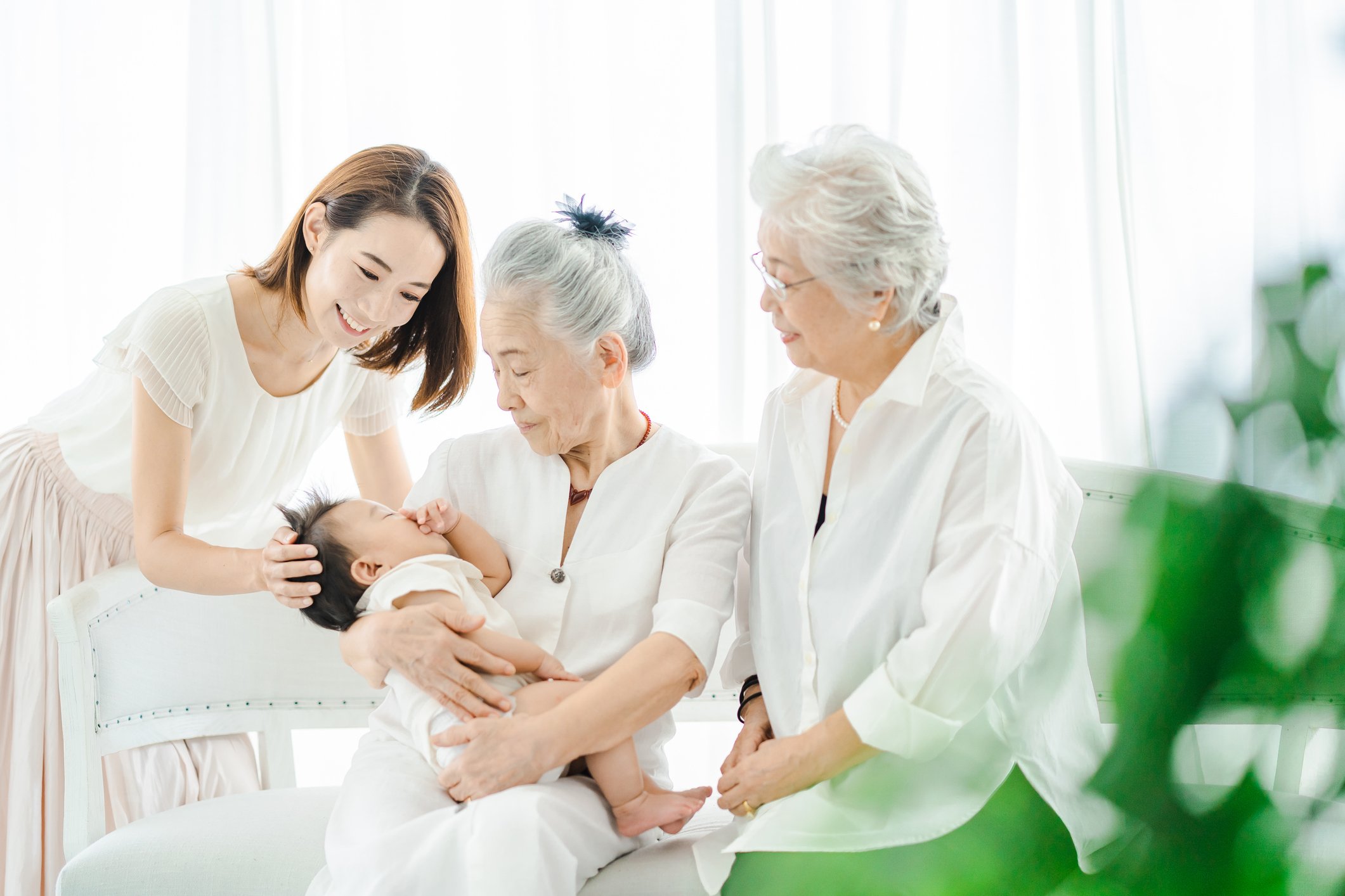 3 generations of women (a brand new mother, a grandmother and great grandmother) are together and looking at a young newborn baby