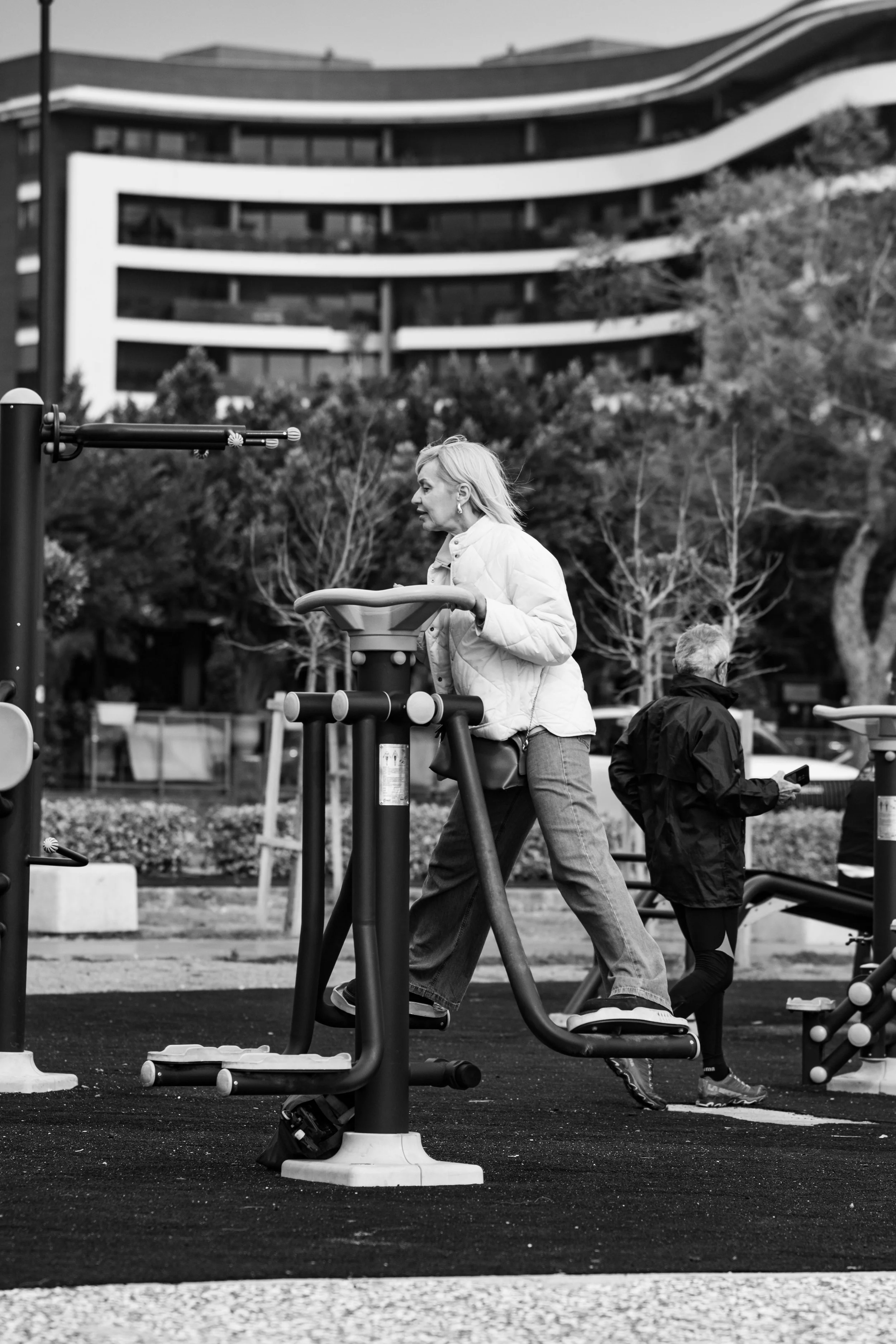 Black and white image of a woman in a park on an outdoor exercise machine