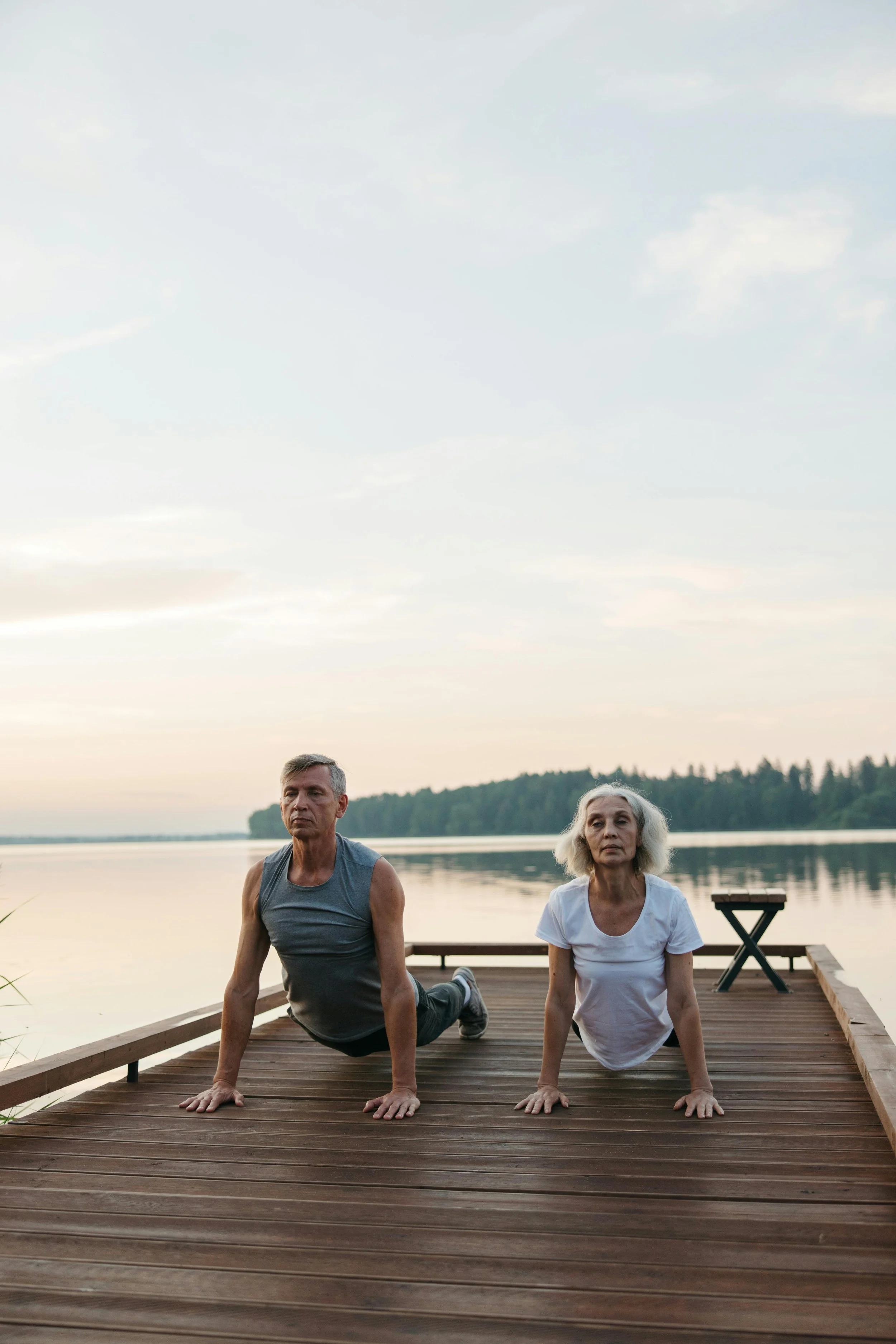 Two seniors on a dock stretching and practicing yoga