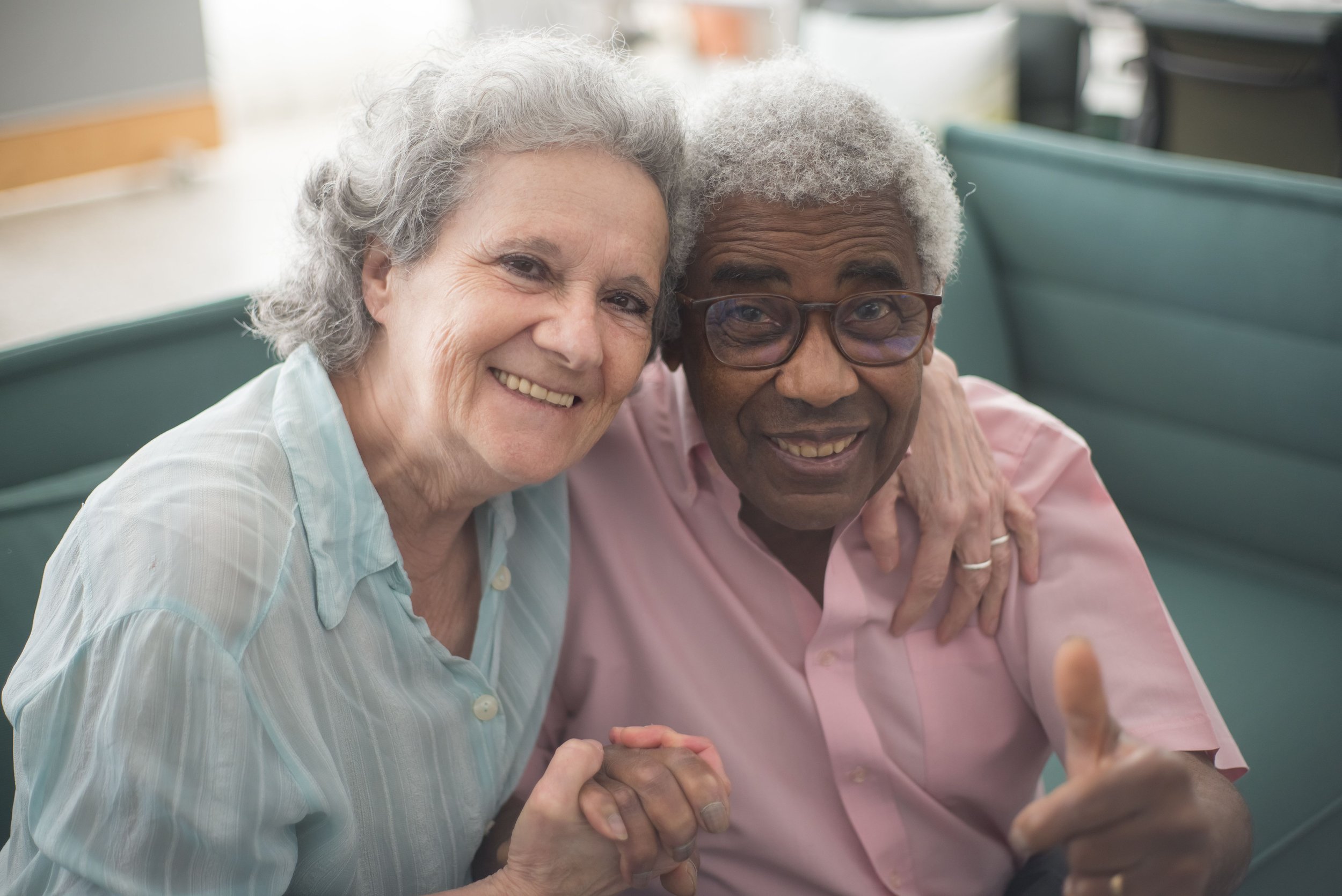 Elderly white woman with grey hair embracing a senior elderly black man, and holding hands lovingly.