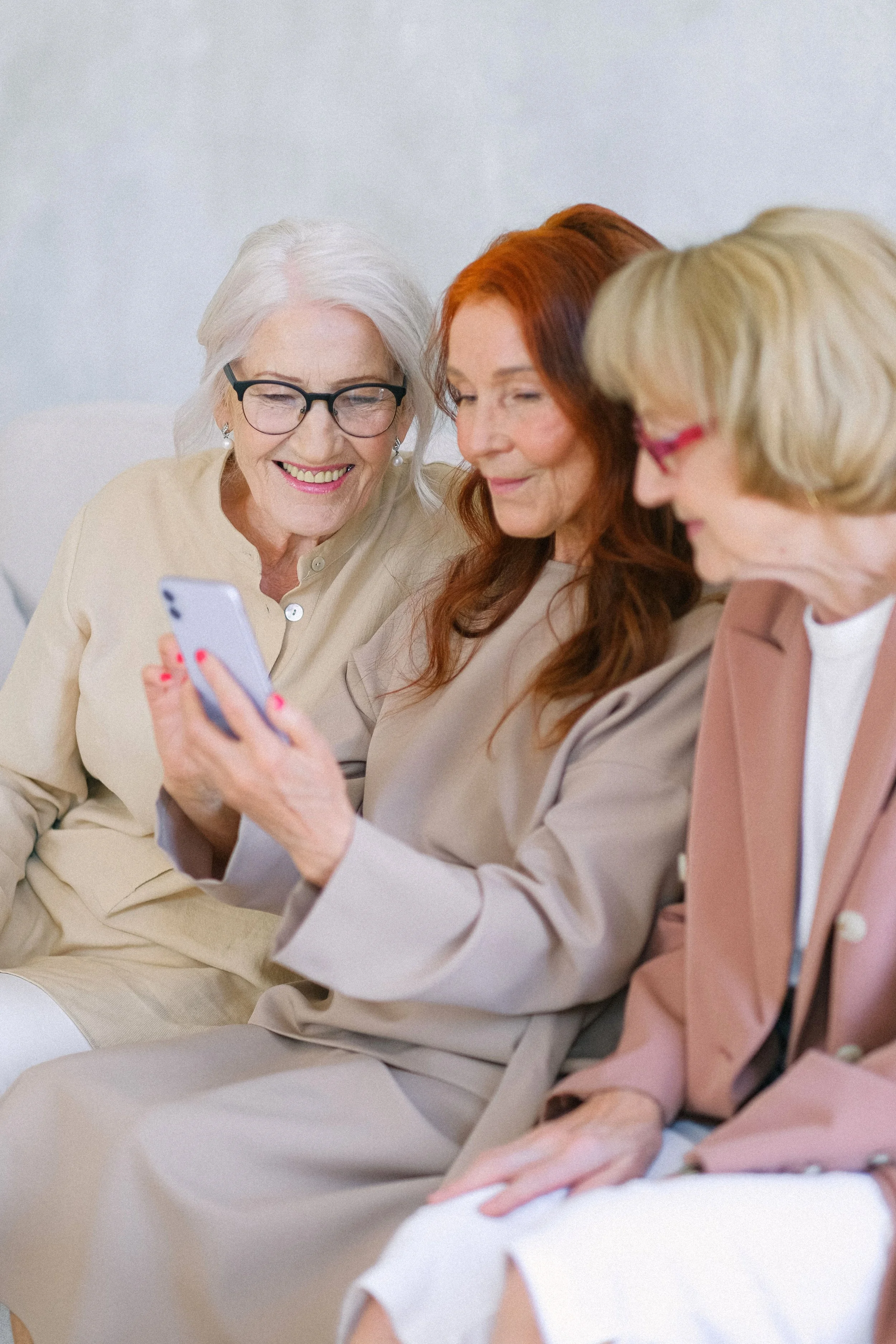 3 50+ year ladies sitting on a couch together looking at a smartphone.