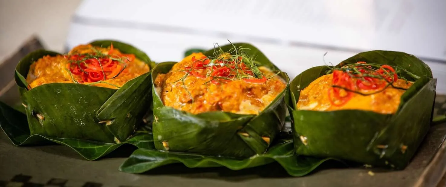 Traditional Cambodian fish amok by Chef Nak, wrapped in banana leaves and topped with red chilies and shredded herbs