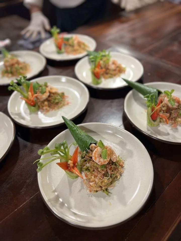 Multiple plates of Thai-style shrimp salad garnished with herbs and vegetables on a dark wooden table.
