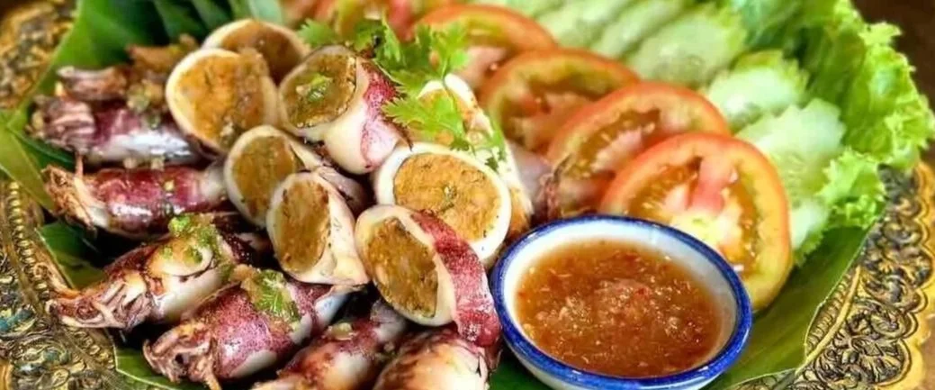 Grilled stuffed squid with Kroeung by Chef Nak, a Cambodian seafood dish served with fresh vegetables and sweet-sour dipping sauce