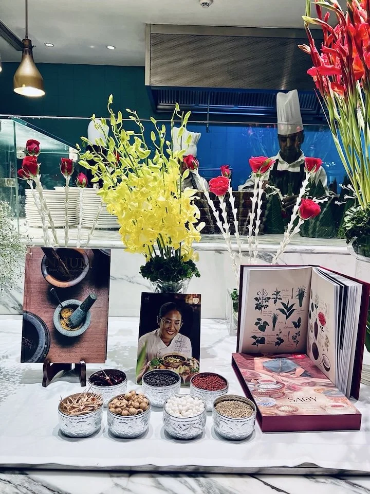 Display of colorful flowers, jars of spices, and a cooking or recipe book at a food or spice shop.