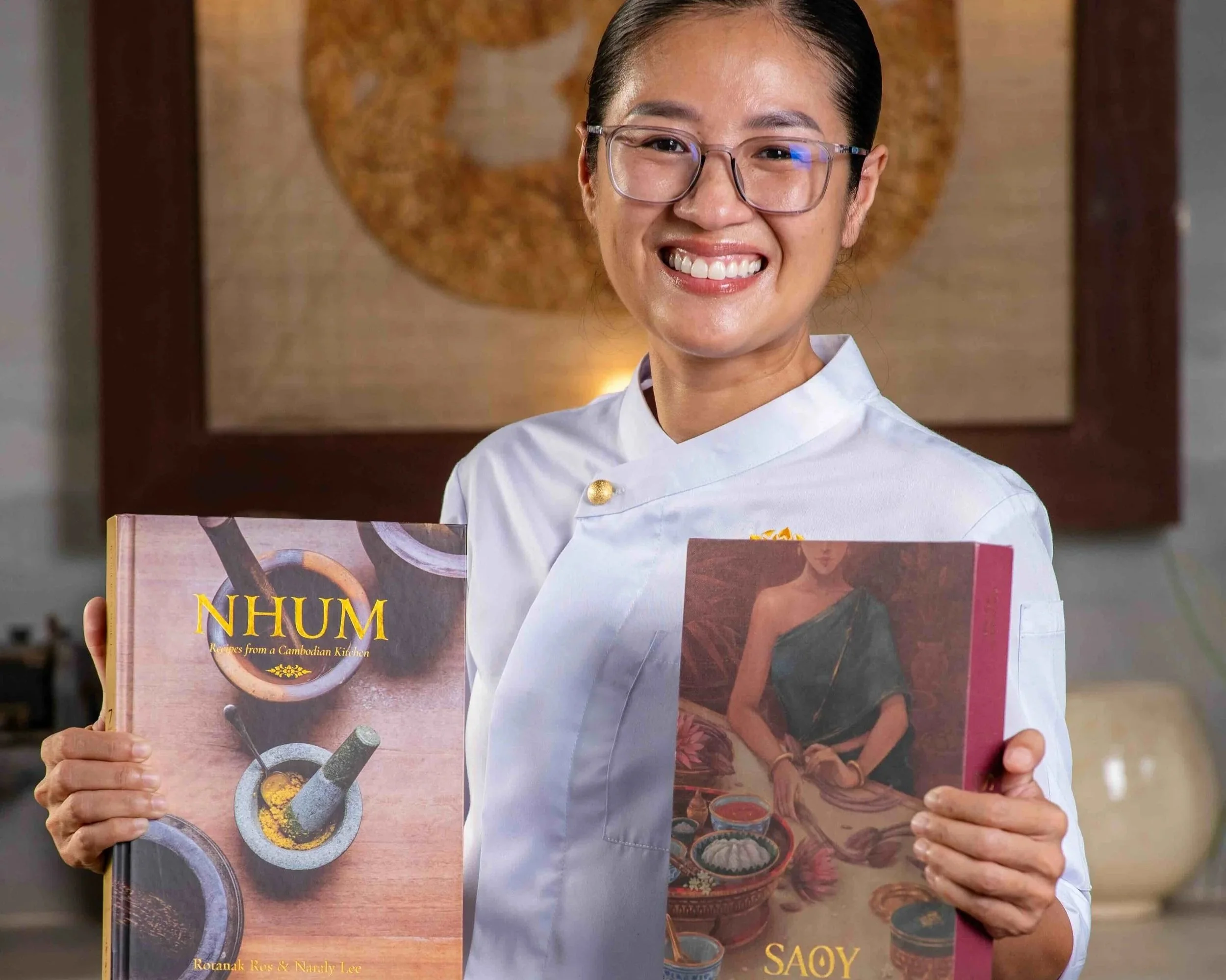 Chef Nak proudly holding her two Cambodian cookbooks, NHUM and SAOY.