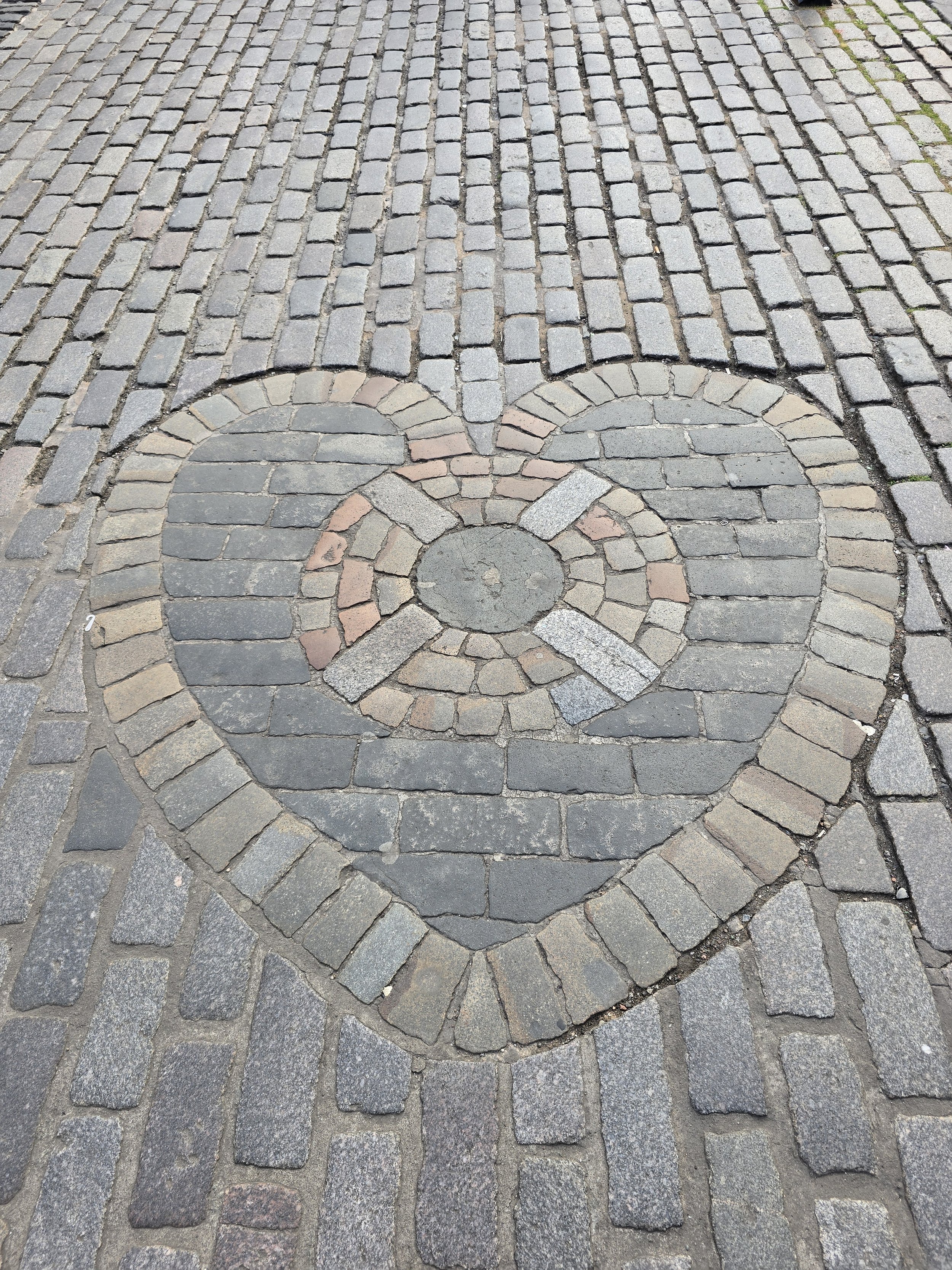 Pavement with cobblestone and brick design forming a smiley face with raised eyebrows and a curved mouth.