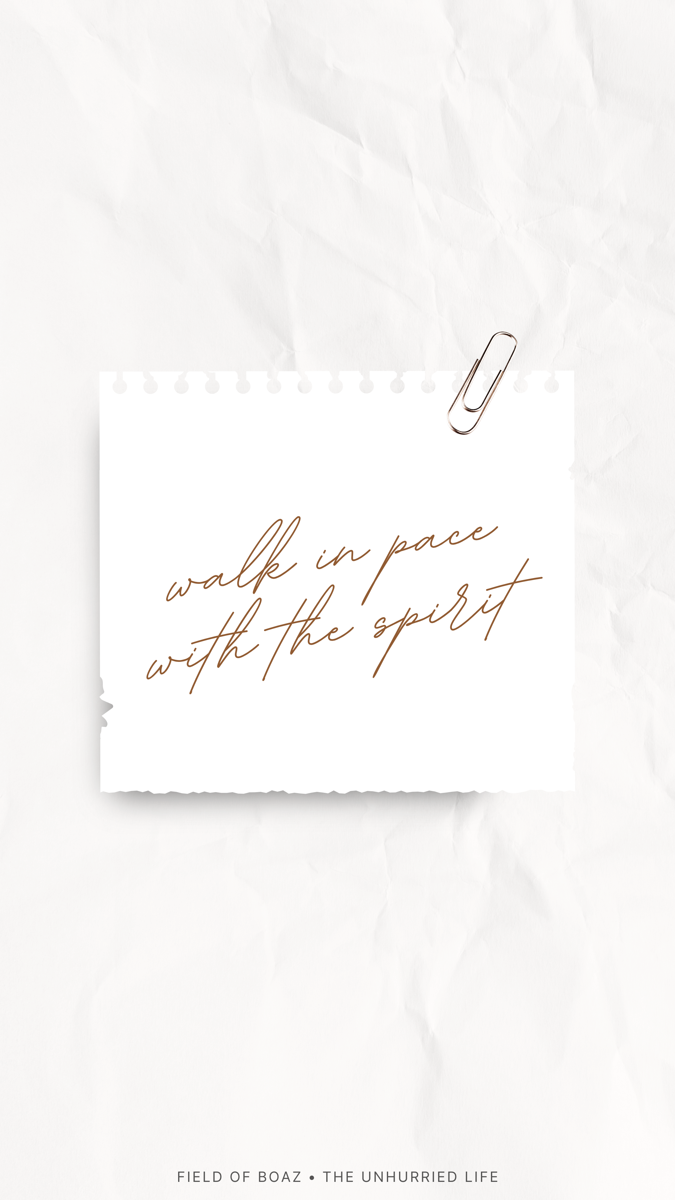 A white paper with the handwritten quote 'walk in pace with the spirit'. The paper is held by a gold paperclip clipped at the top right corner, and is placed on crumpled white paper background. The text at the bottom reads 'FIELD OF BOAZ • THE UNHURR