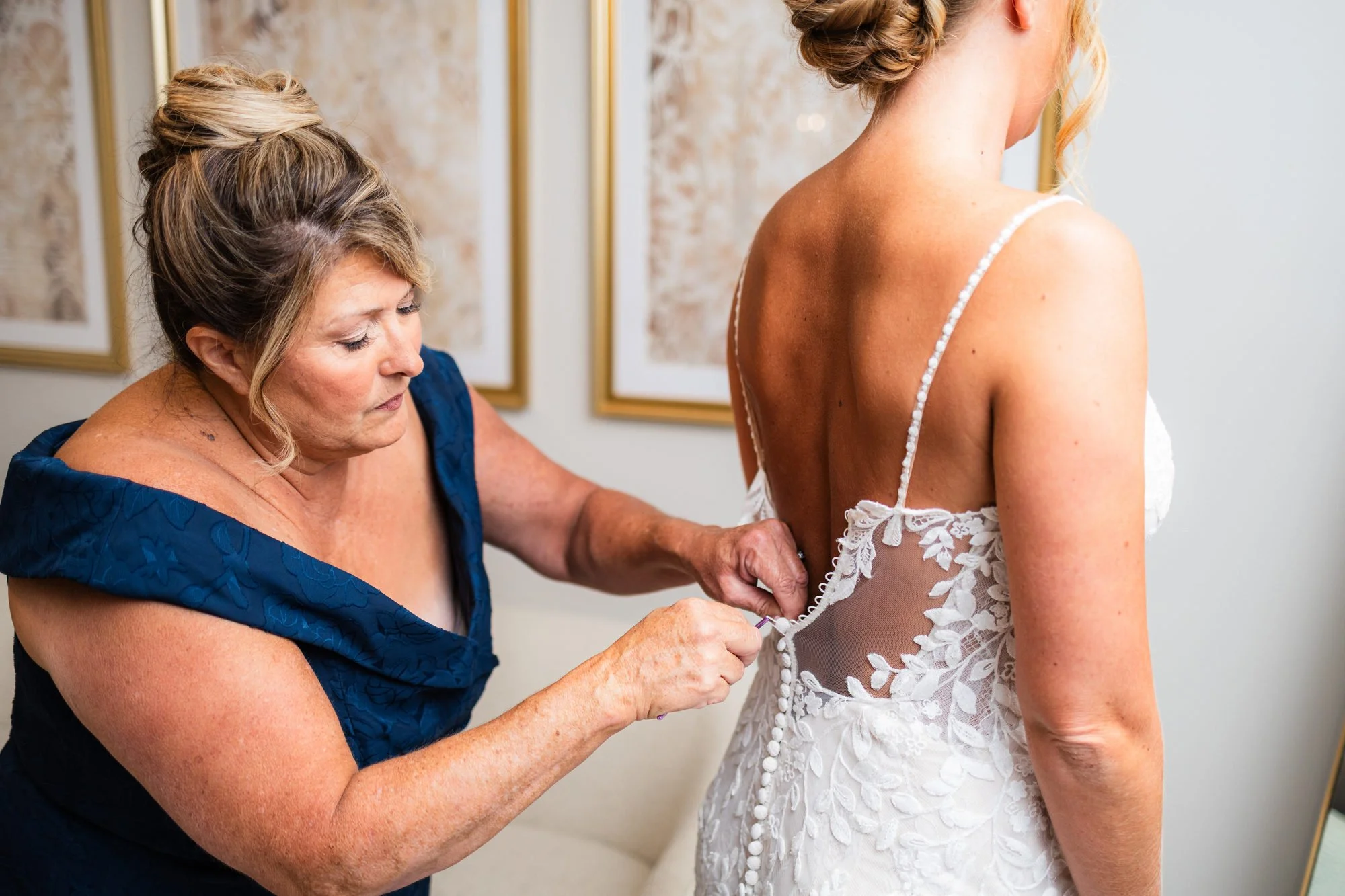 Mother of the bride buttoning the back of the wedding dress at Greenbrier Farms