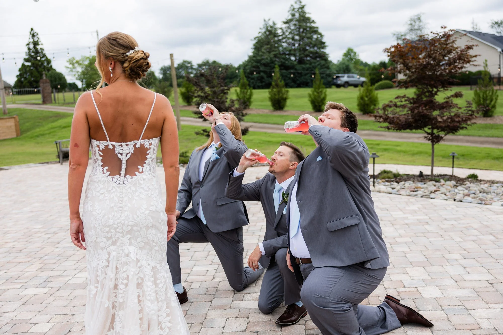 Groomsmen kneeling and chugging drinks when they see the bride on the patio at Greenbrier Farms