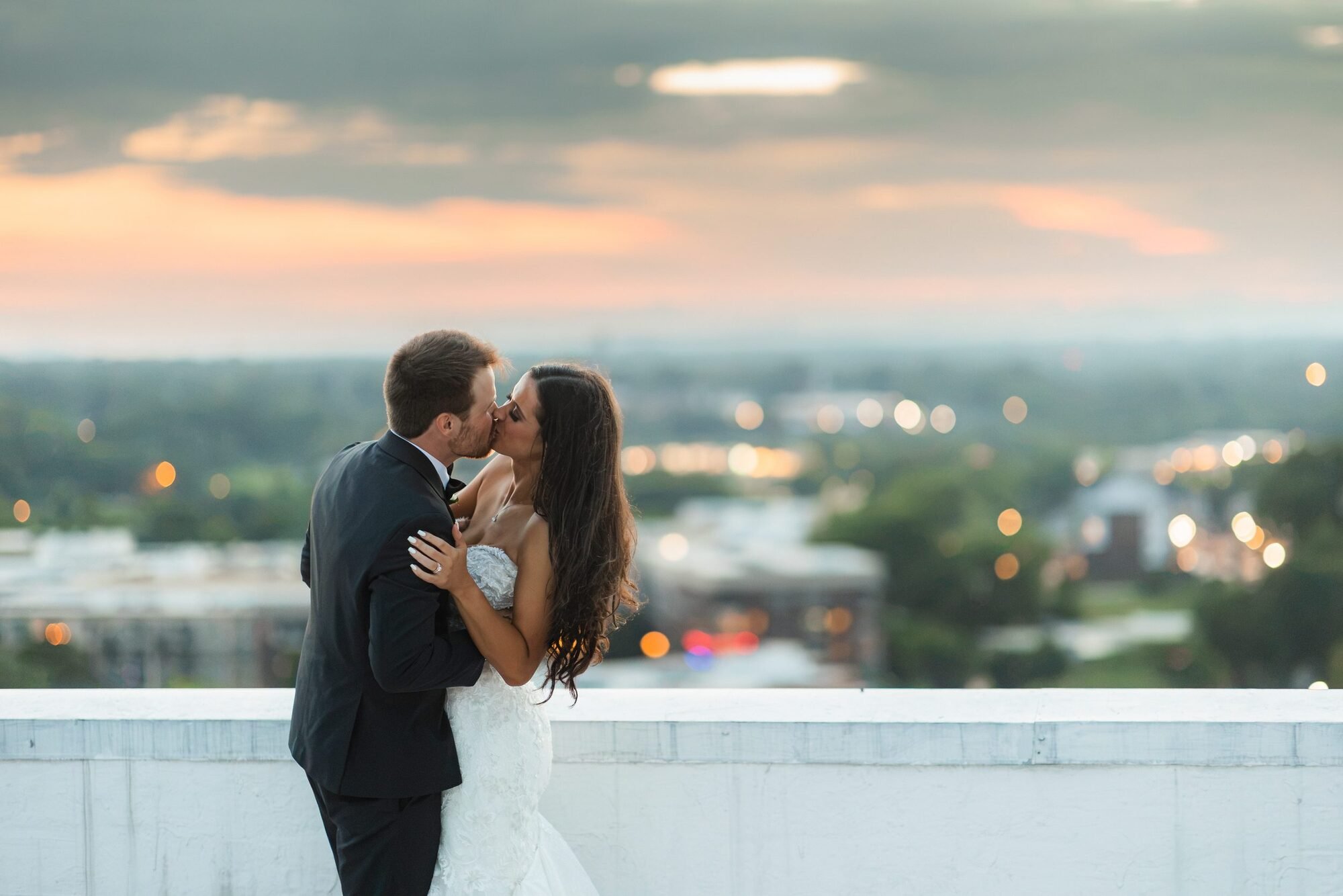 Bride and groom kissing on the Westin Poinsett rooftop with downtown Greenville, SC at sunset