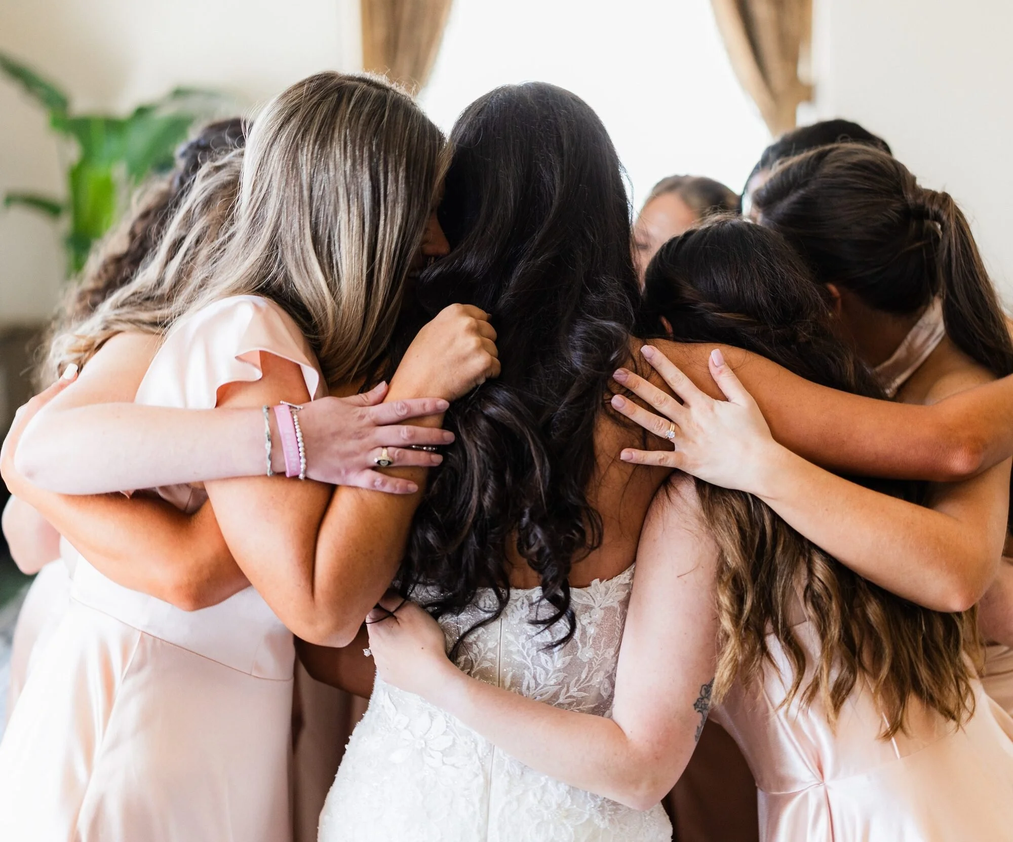 Bride with hair and makeup by Bombshell Lounge hugging her bridesmaids at the Westin Poinsett