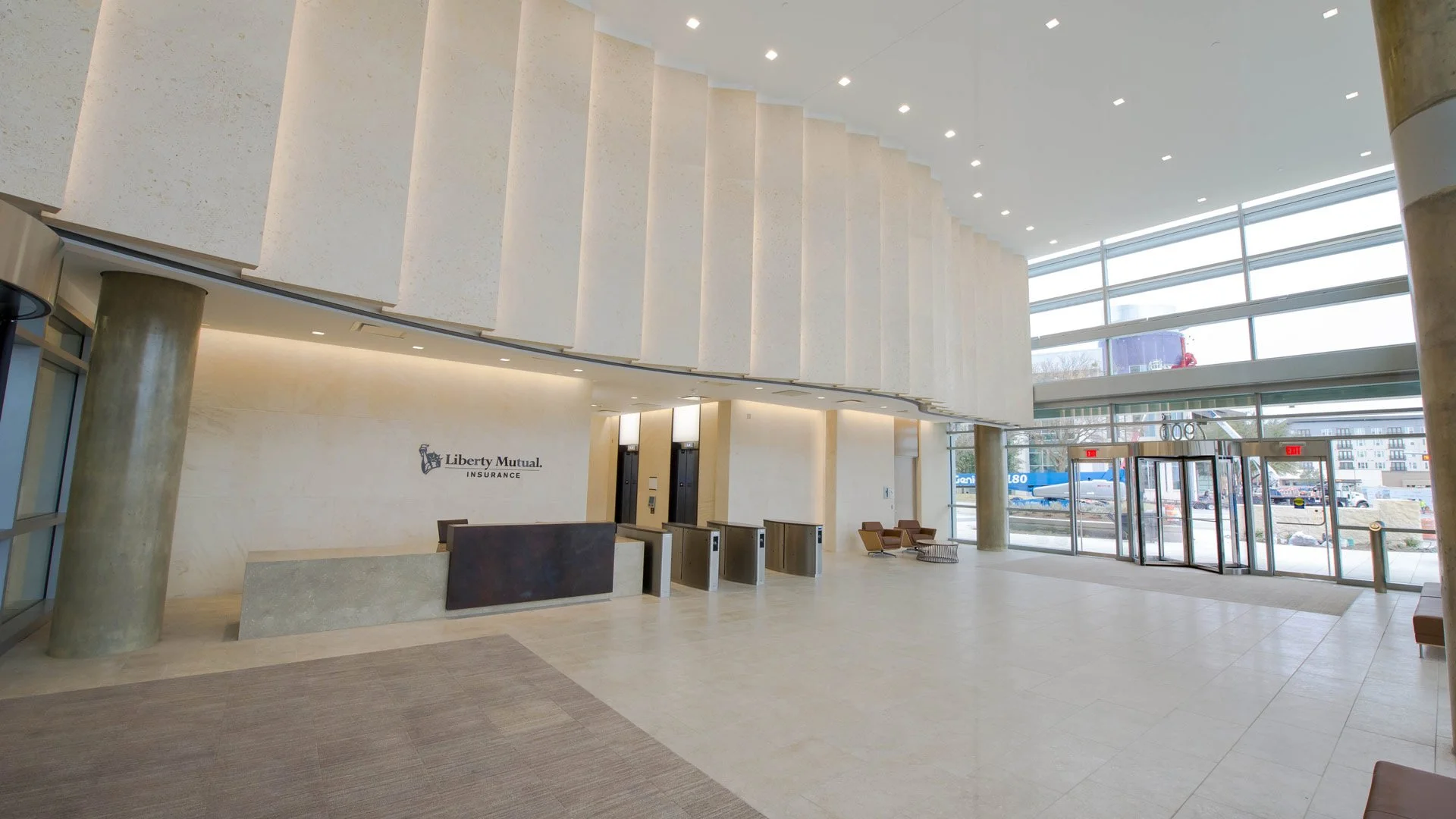 Lobby area of Liberty Mutual Insurance office with reception desk, elevator doors, seating area, and large glass entrance with automatic sliding doors.