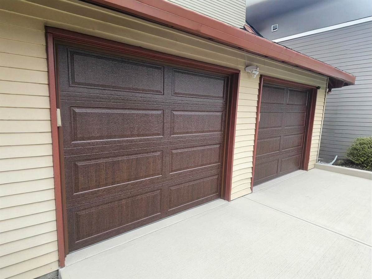 Two brown garage doors on a beige house with a concrete driveway.