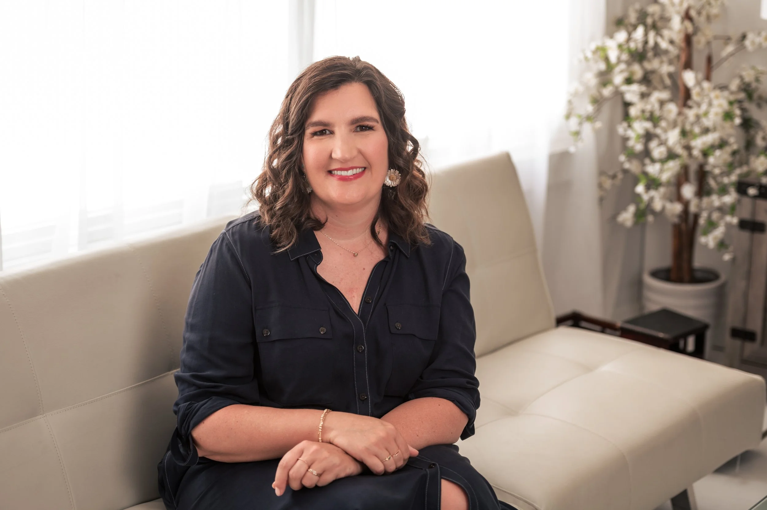 Woman sitting on a white sofa, smiling, with floral decoration in the background.