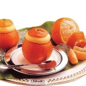 Oranges with some peeled and sliced, arranged on a silver tray with a spoon and a green leafy cloth.