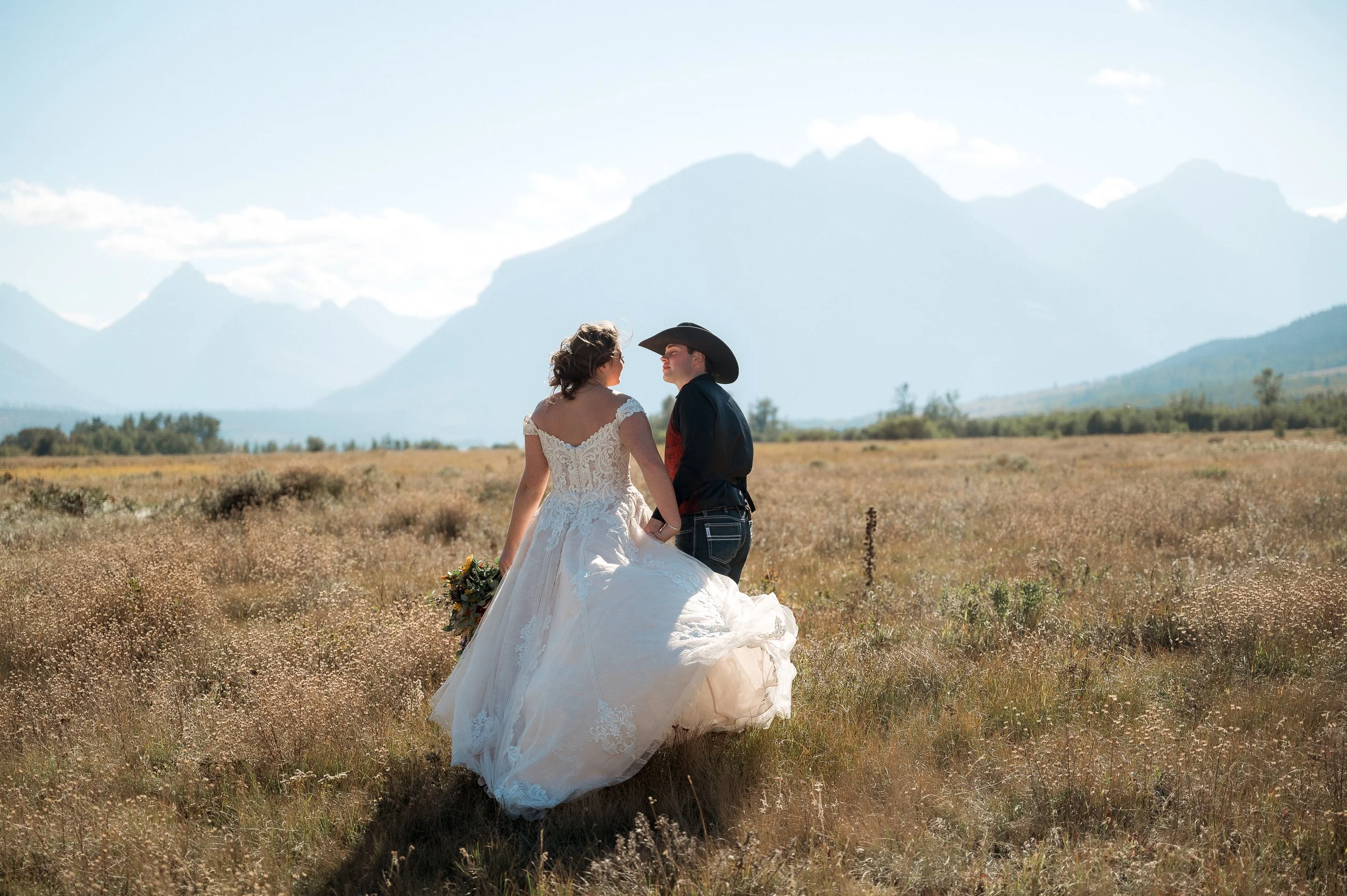 Bride and groom standing in a grassy field with mountains in the background