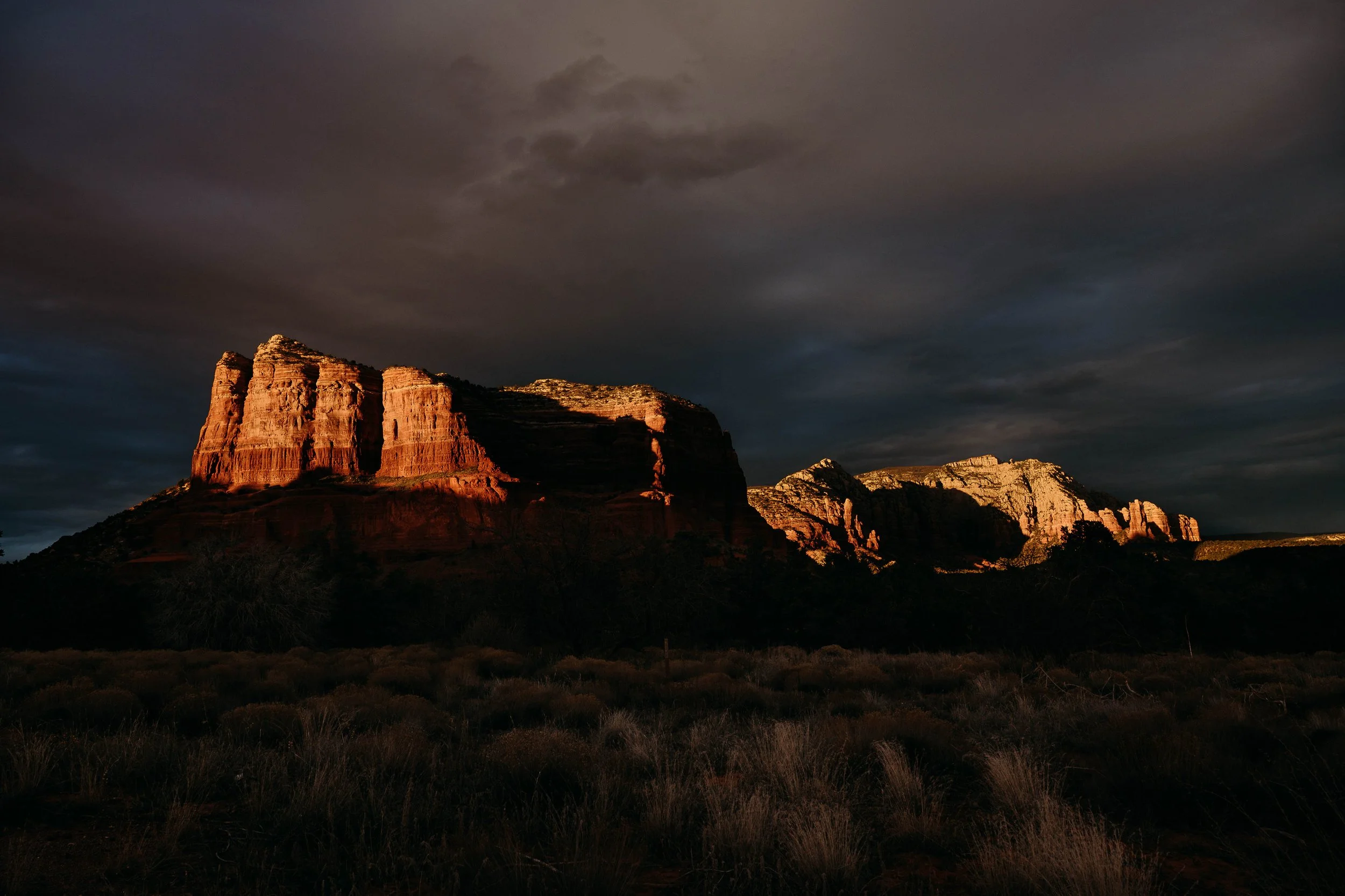 Reddish rock formations under dark, cloudy sky at twilight.