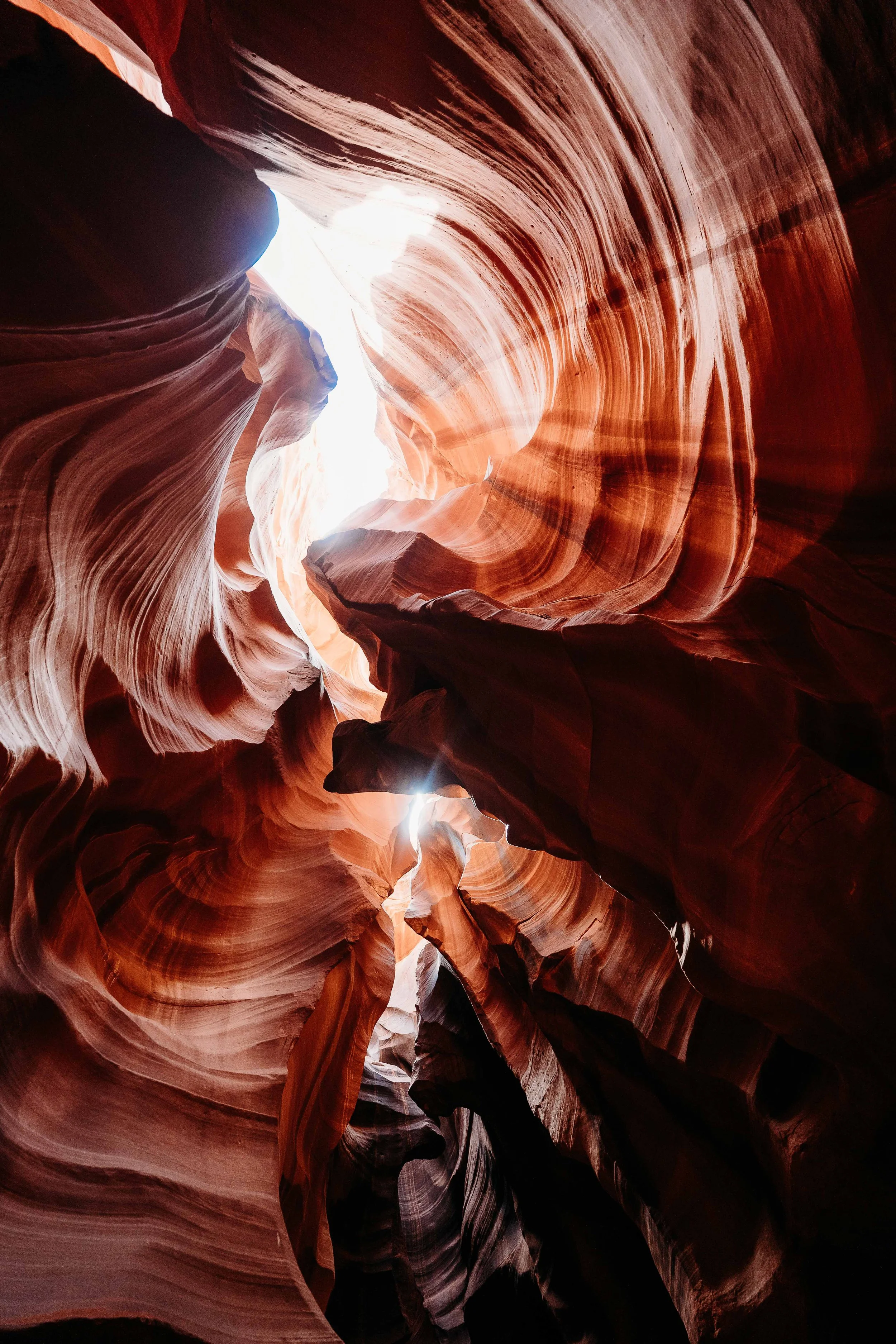 Inside view of a narrow slot canyon with smooth, flowing sandstone walls in shades of orange and red, with light streaming from above.