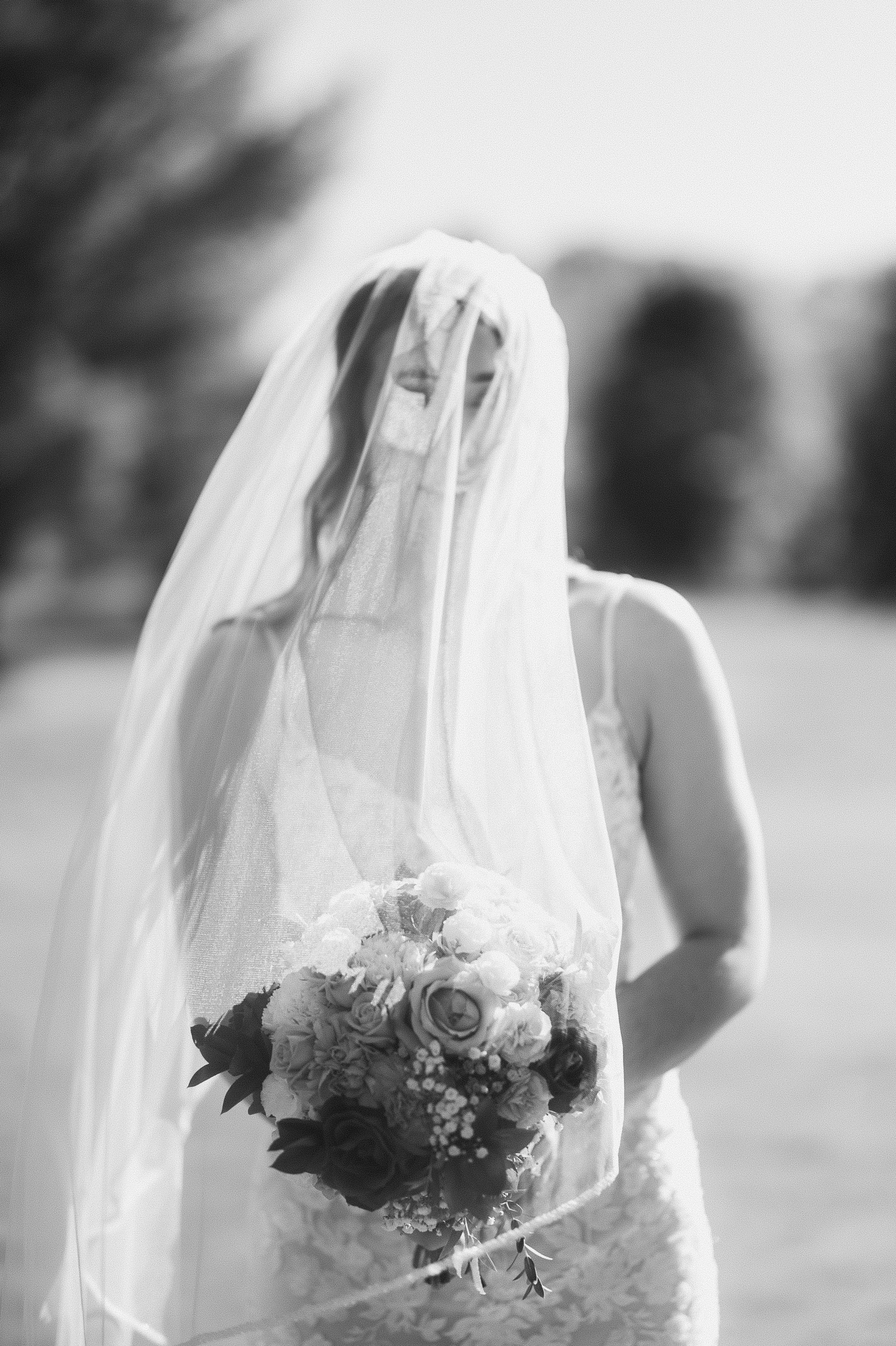 A bride wearing a wedding dress and veil holding a bouquet of flowers outdoors.