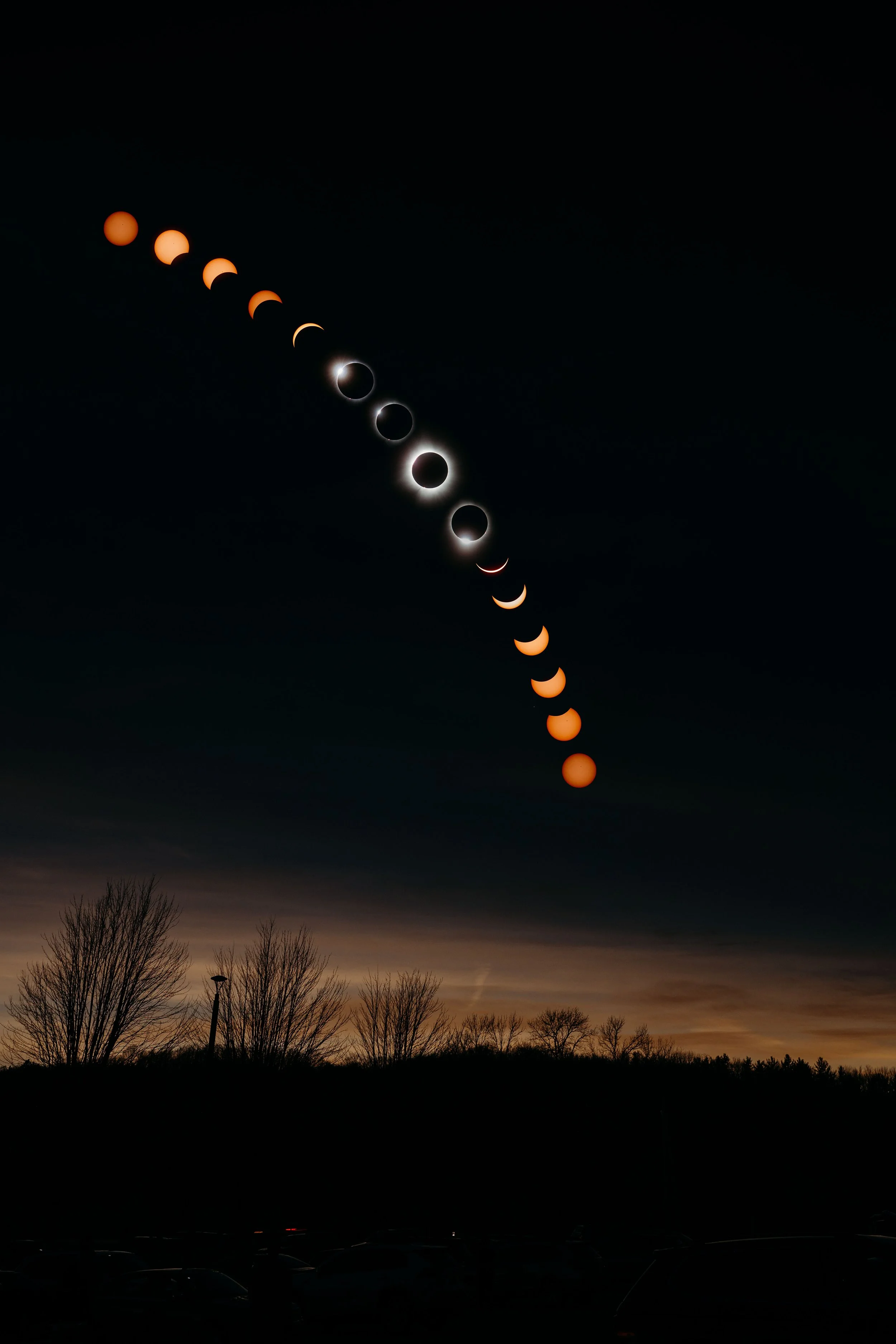 Sequence of images showing a solar eclipse with the moon passing in front of the sun, creating a ring of fire effect, observed above a landscape with leafless trees at dusk.