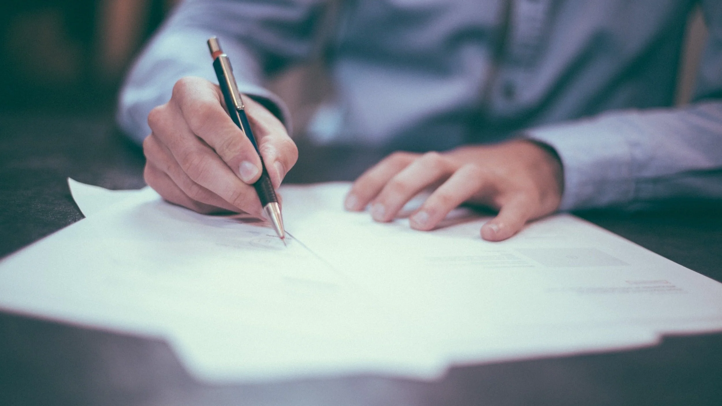 Don’t Get Burned On Your Software Development Agreements: photograph showing a man's hands holding a pen and writing something on a stack of papers