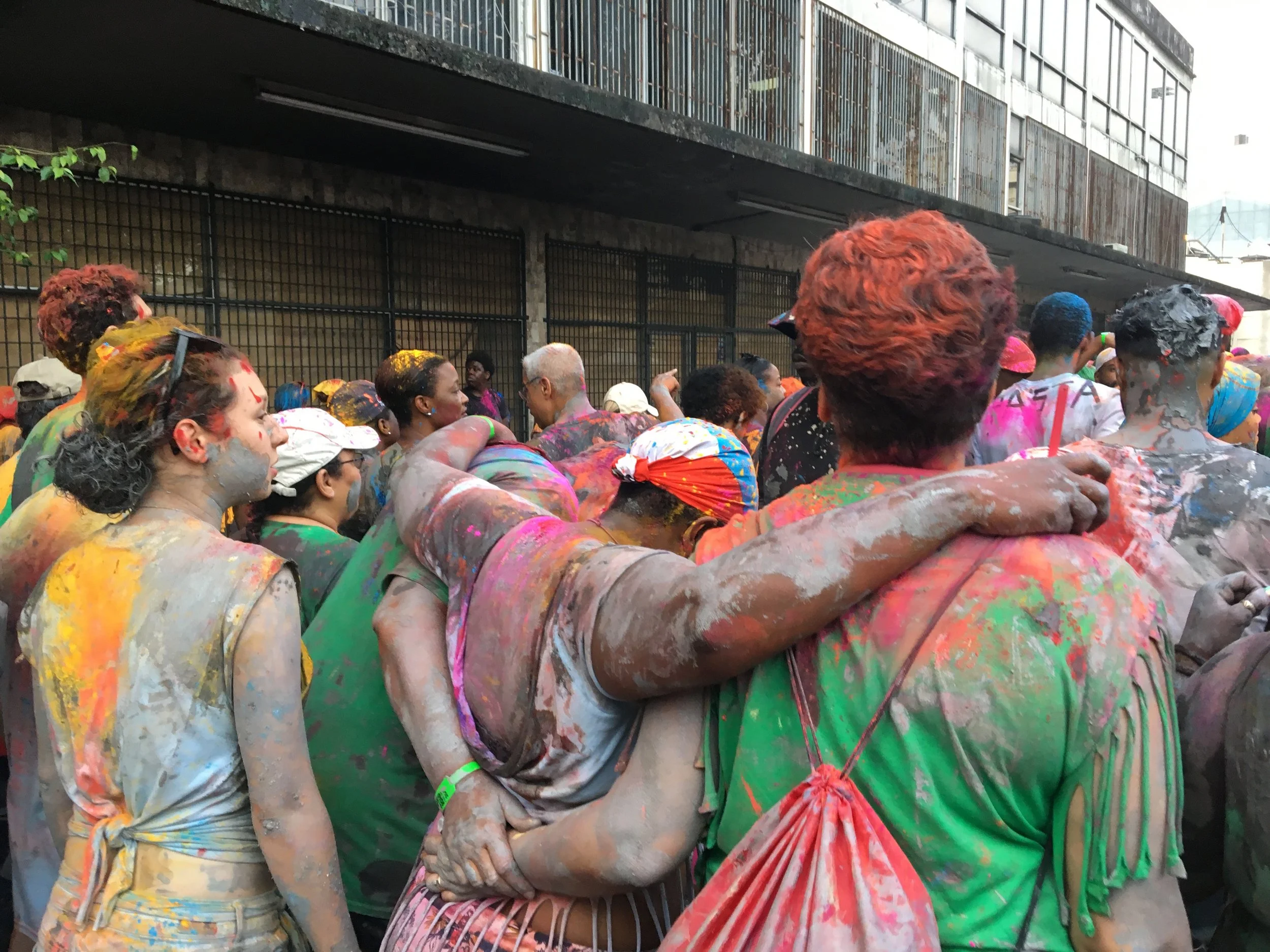 People celebrating Holi, the festival of colors, showing colorful powder on their clothes and skin, with some hugging and some looking around.