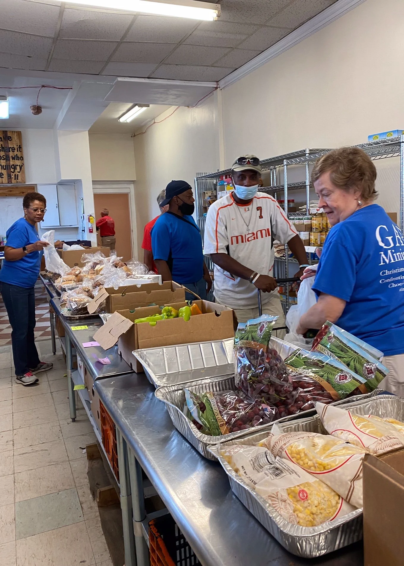 People gather beside tables of fresh produce and bread at GAP’s food pantry.