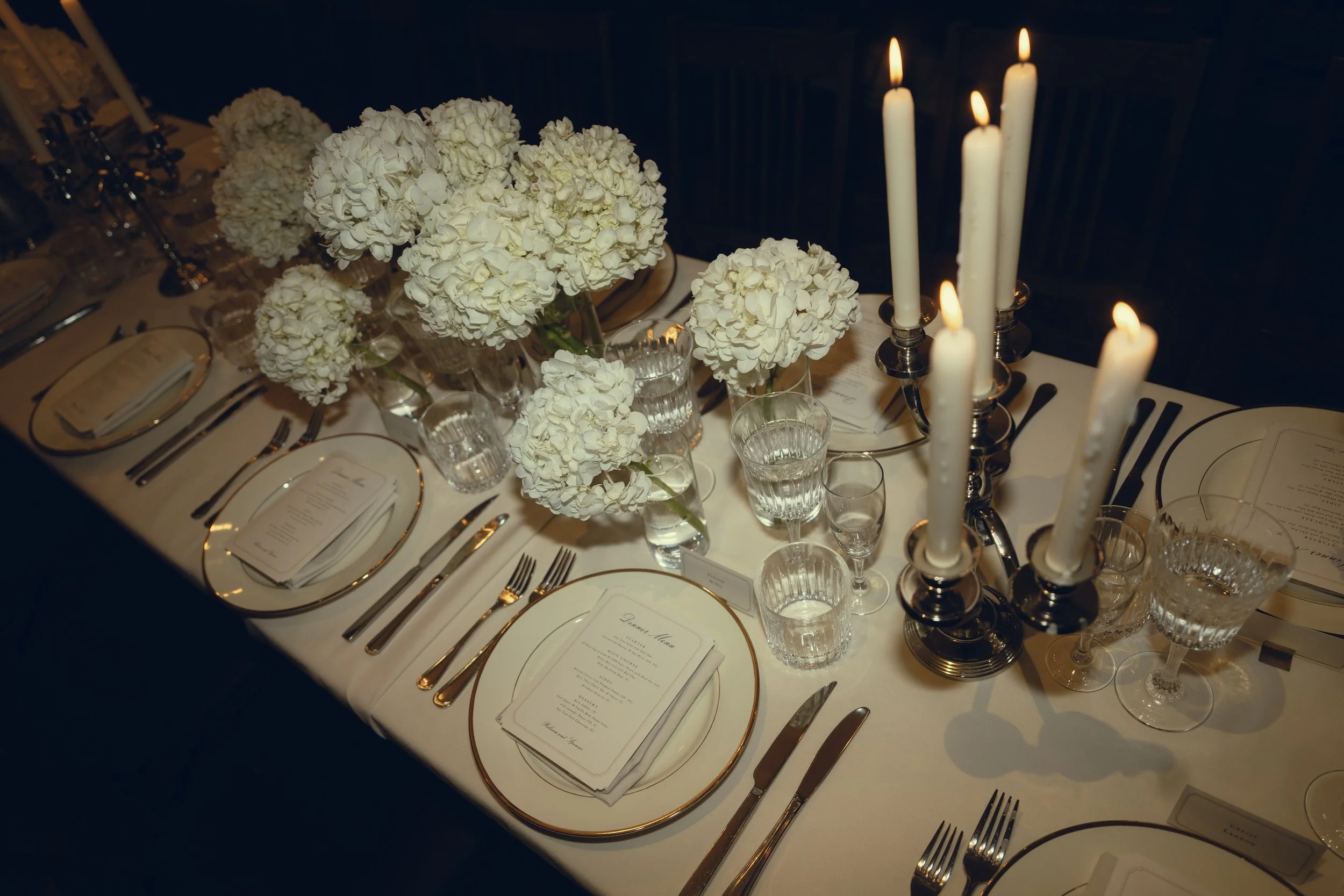Elegant dining table set with white floral centerpieces, tall candles, wine glasses, and silverware.