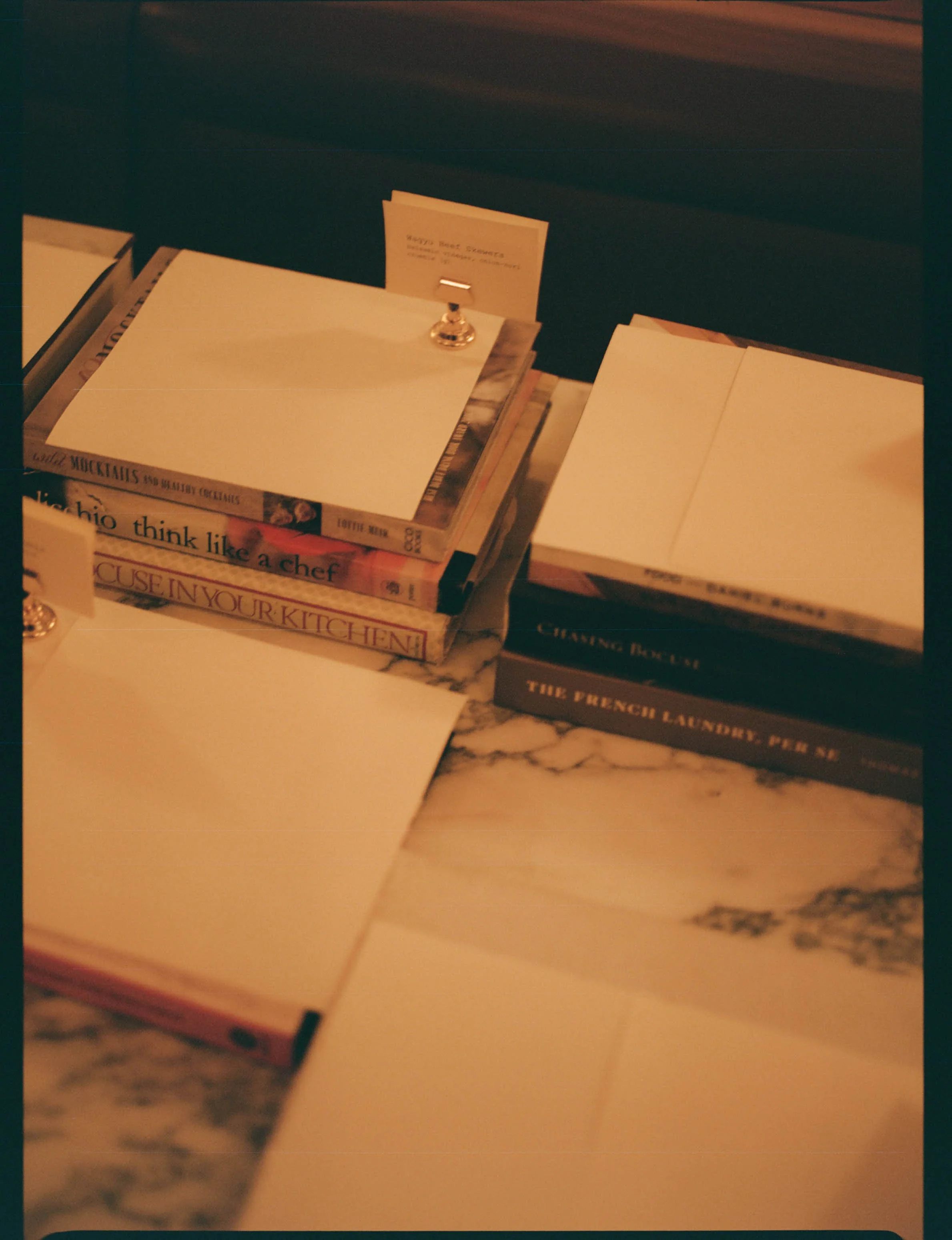 Stack of empty notebooks and magazines on a marble surface, with some note cards and a silver clip.