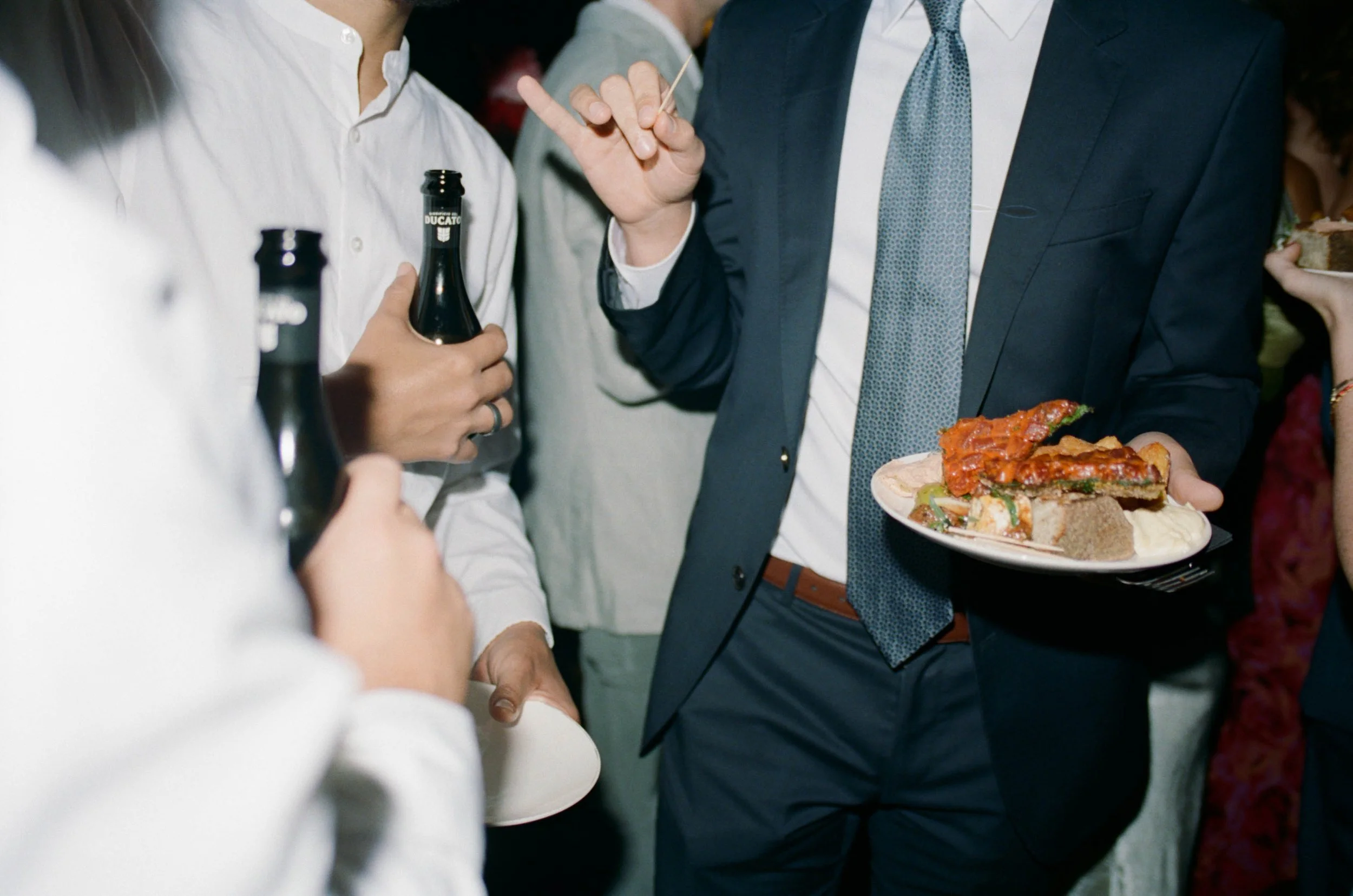 People gathered at a social event, engaging in conversation. One person is holding a plate with slices of pizza and sides.