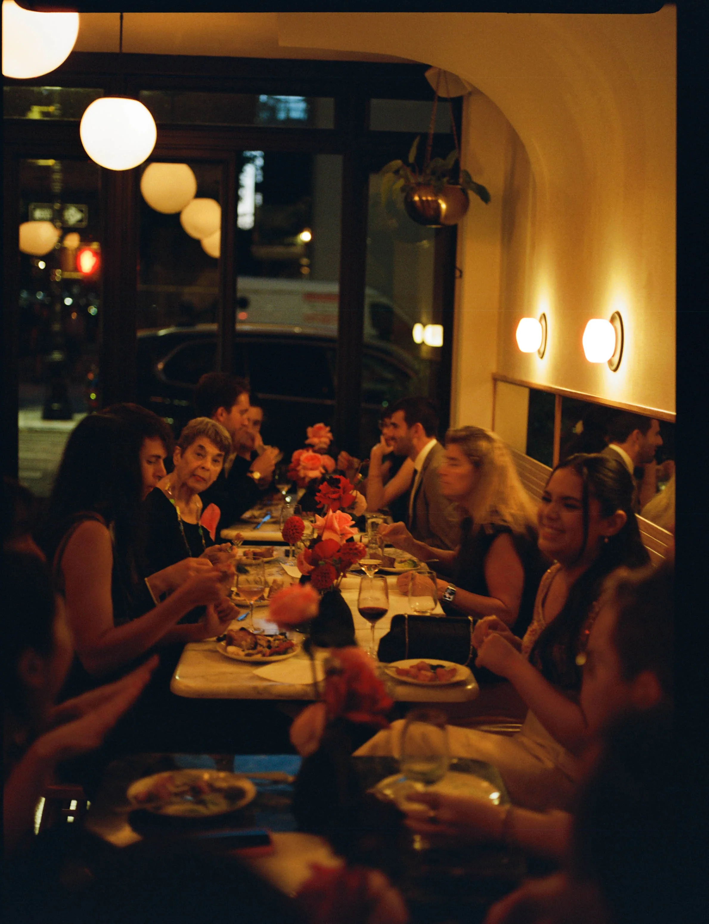 People dining together at a long dinner table in a warmly lit restaurant during the evening.