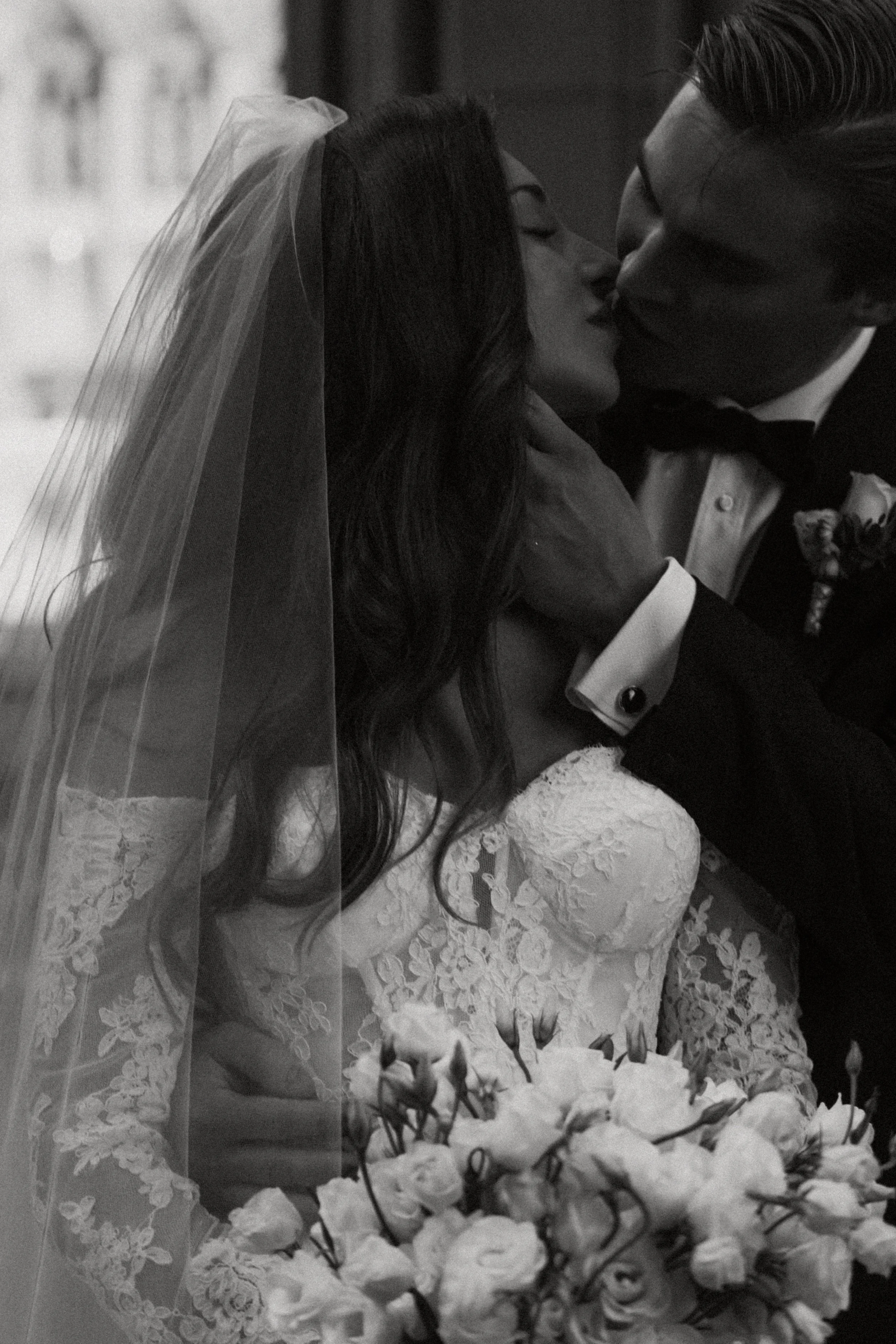 Black and white photo of a bride and groom kissing, with the bride holding a bouquet of roses.