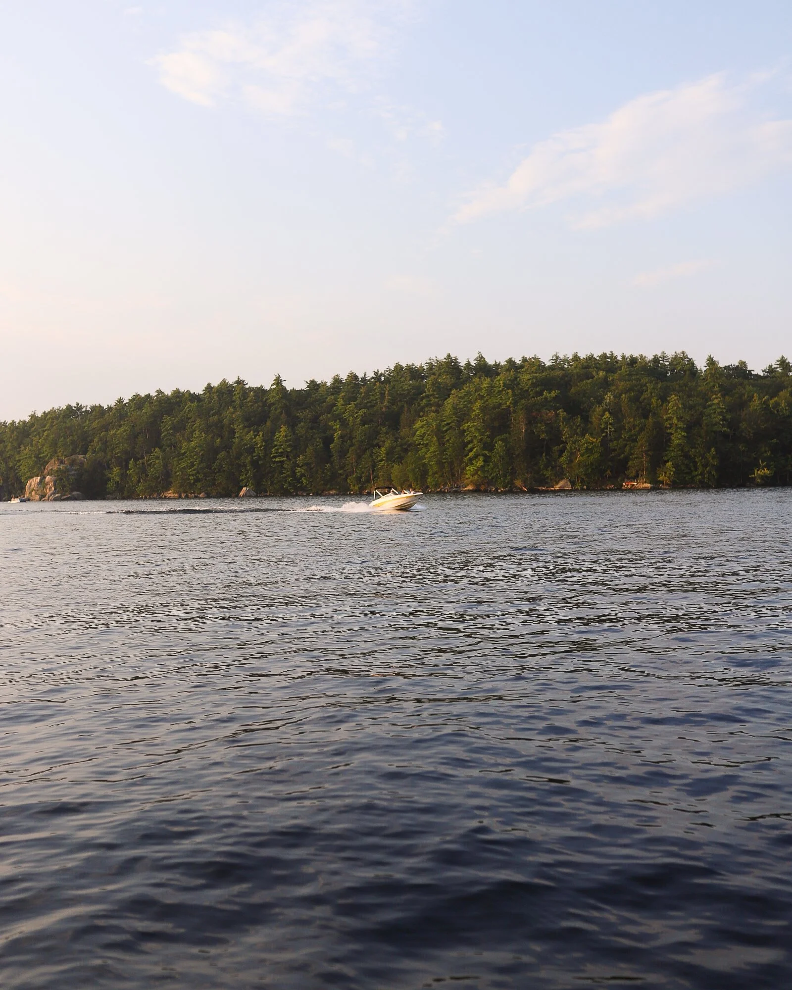 A boat cruising on a body of water with a tree-covered island in the background under a partly cloudy sky.
