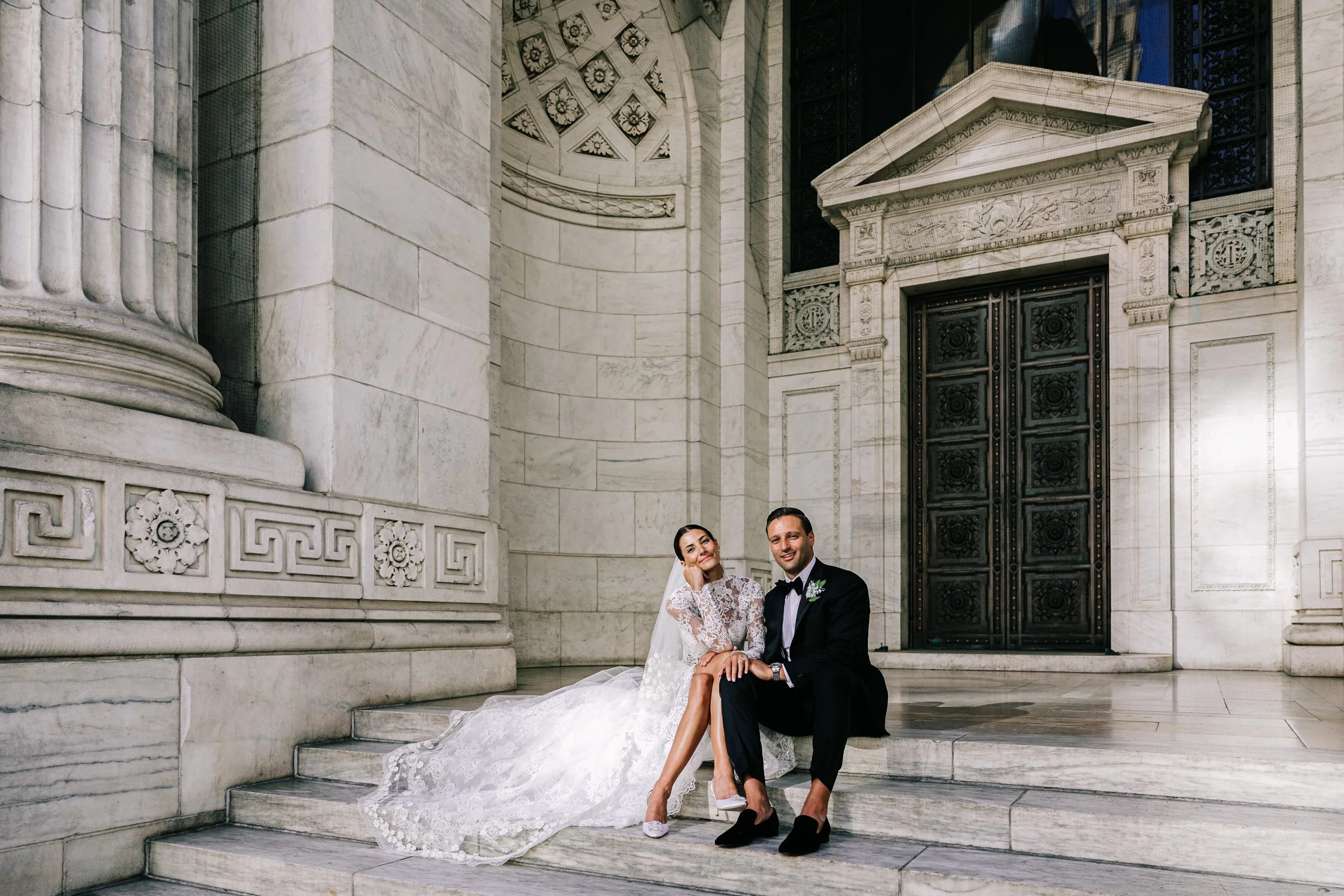 Bride and groom sitting together on the grand exterior steps of the New York Public Library, NYC wedding