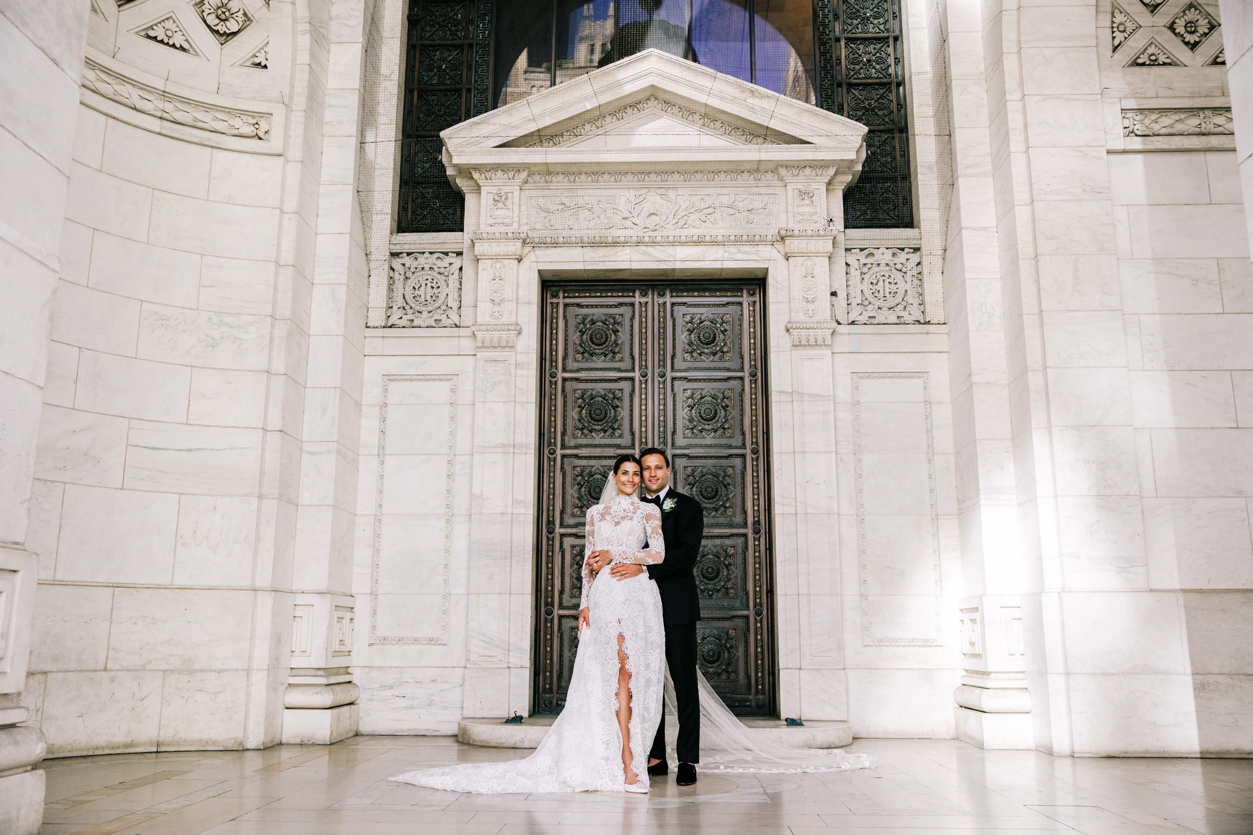 Bride and groom posing together in front of the ornate bronze entrance doors of the New York Public Library, NYC wedding