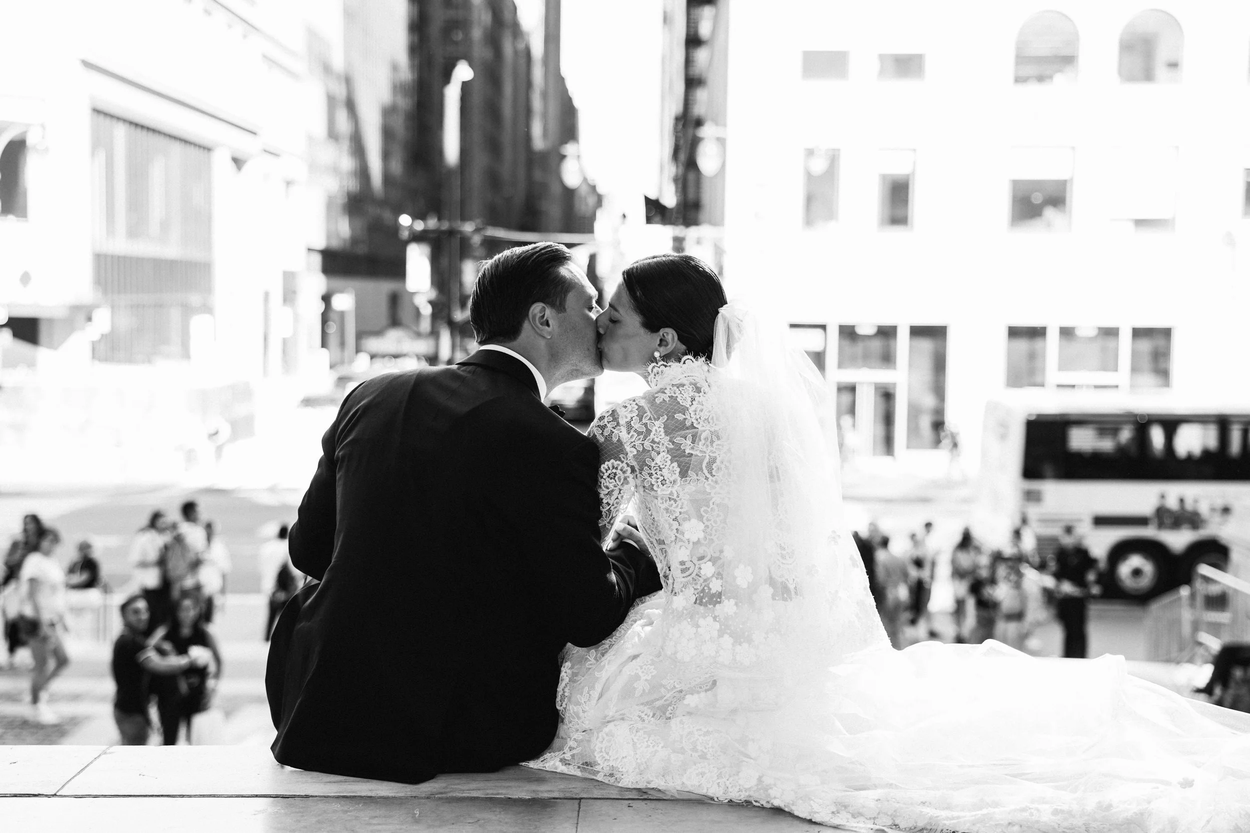 black and white photo of bride and groom standing on the exterior steps of the New York Public Library with the ornate columns and bronze doors behind them