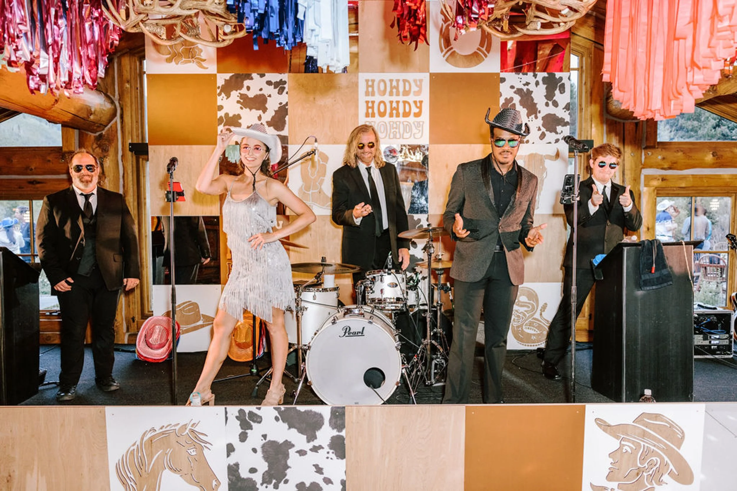 Guests dancing in front of live band at Pine Creek Cookhouse wedding reception with Hondy Hondy signs and colorful streamers in Colorado