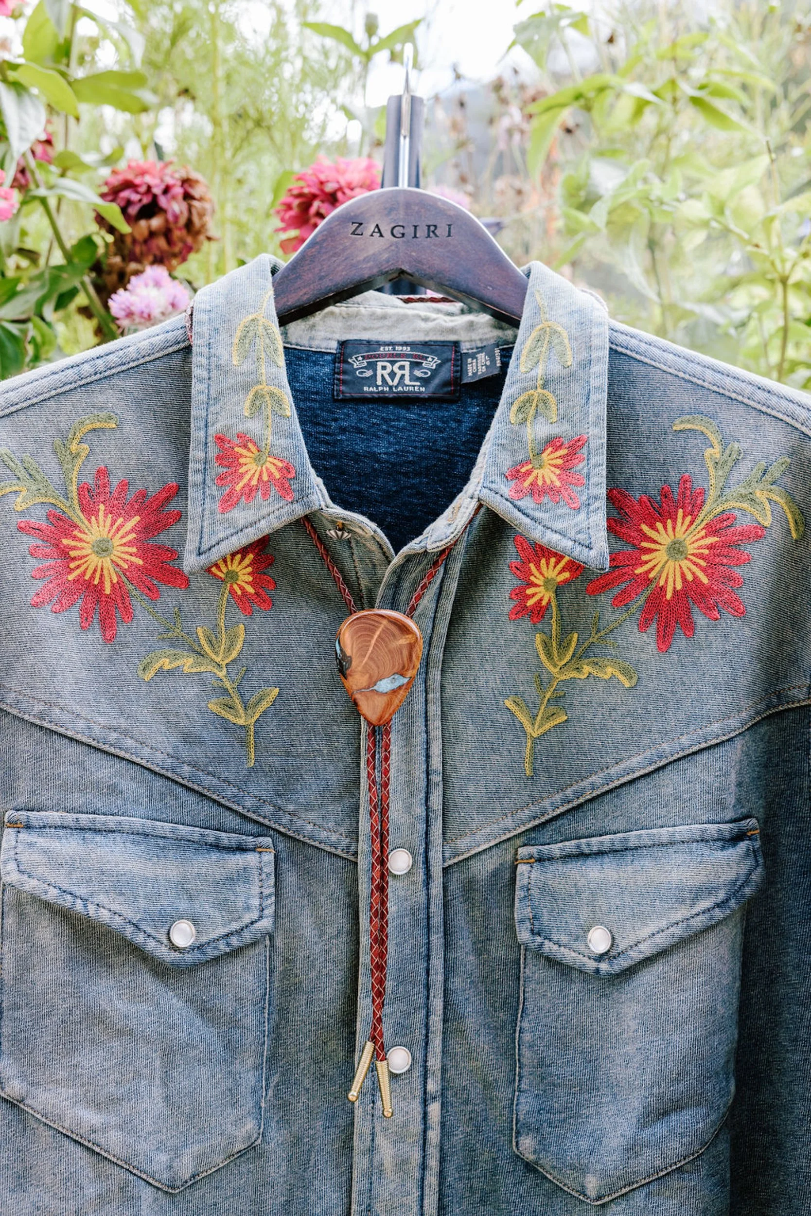 Denim western shirt with embroidered floral detail and orange bolo tie on a hanger, groom attire detail for the rodeo disco reception at Pine Creek Cookhouse
