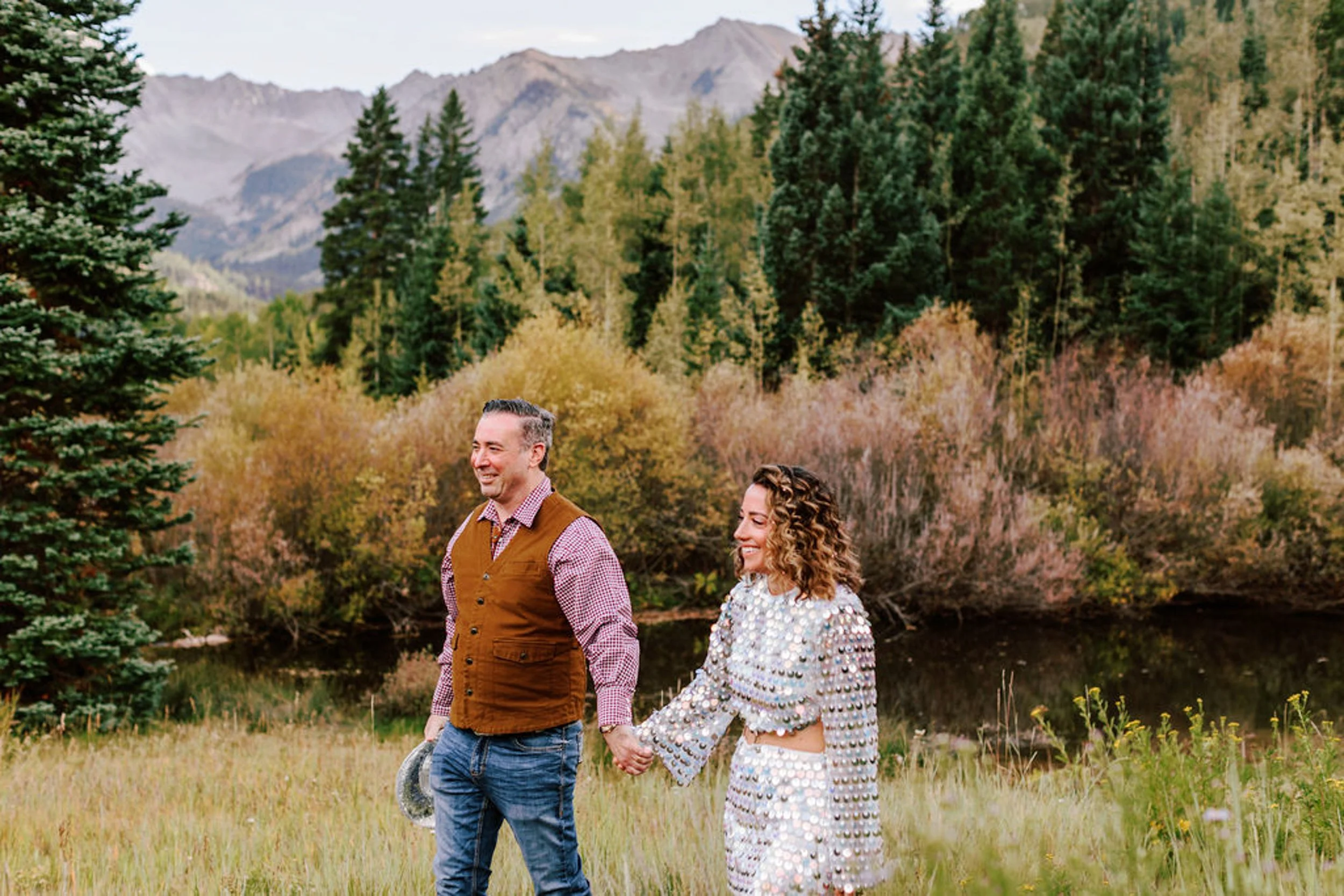Wedding couple walking hand in hand through autumn meadow with pine trees and Castle Creek Valley mountains, Pine Creek Cookhouse wedding photography