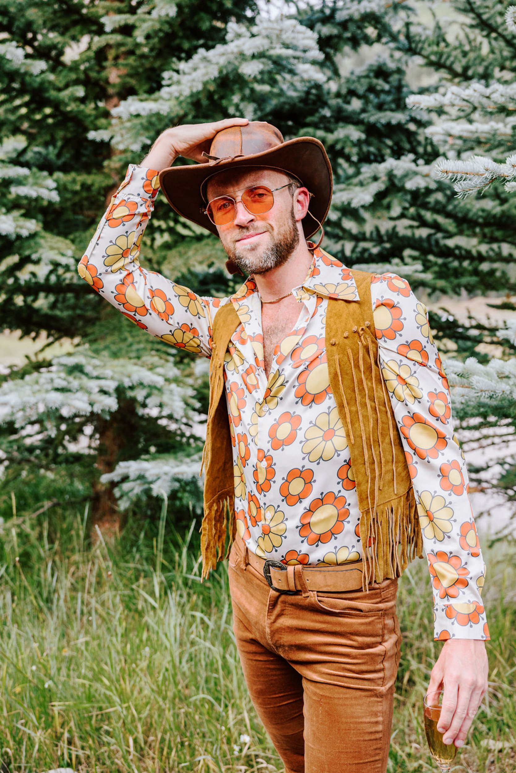 Groom in floral western shirt and fringe vest tipping his cowboy hat, rodeo disco wedding portrait at Pine Creek Cookhouse Aspen Colorado