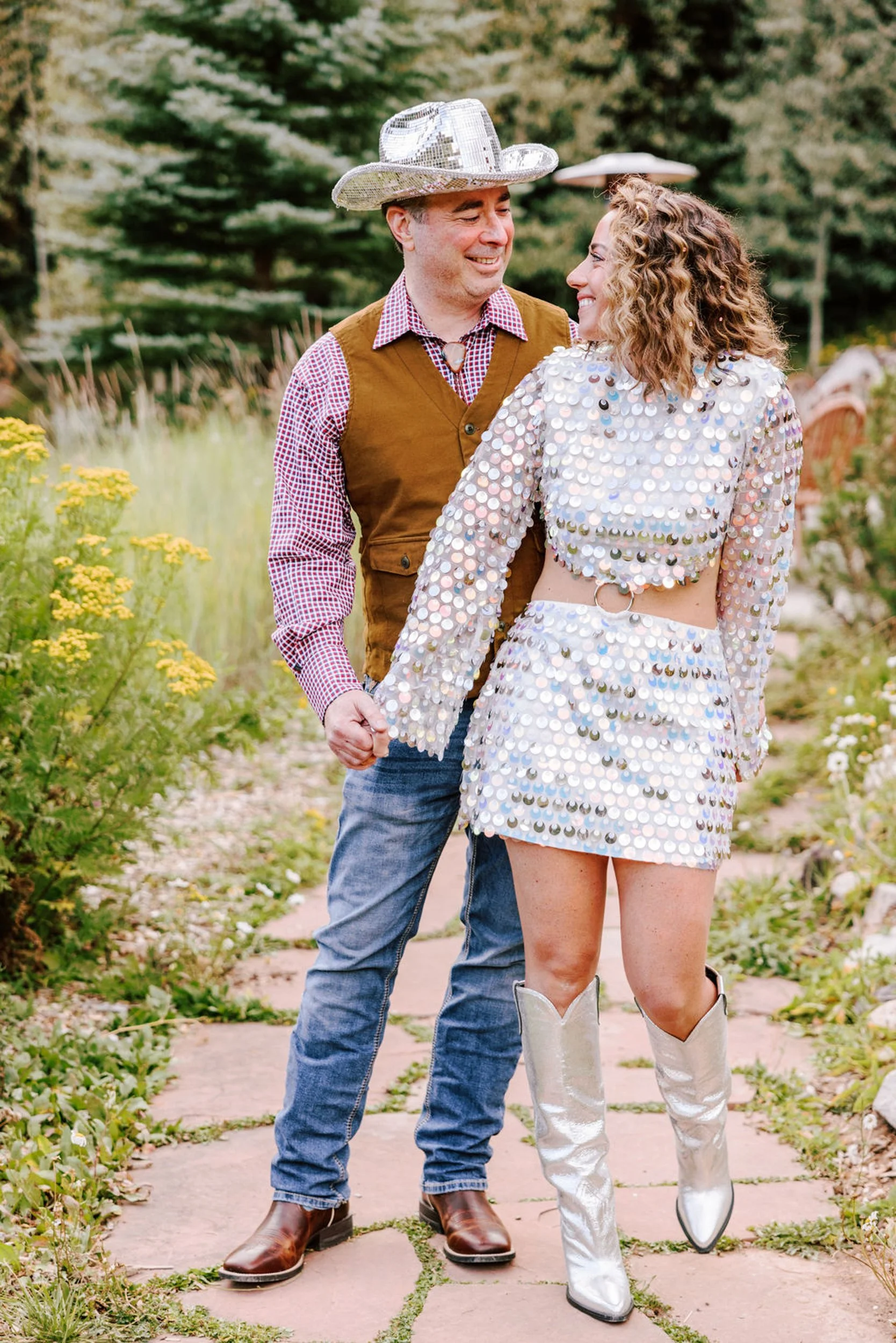 Bride in silver sequin two-piece and white cowboy boots with groom in western hat and vest at their Pine Creek Cookhouse rodeo disco reception, Aspen area wedding