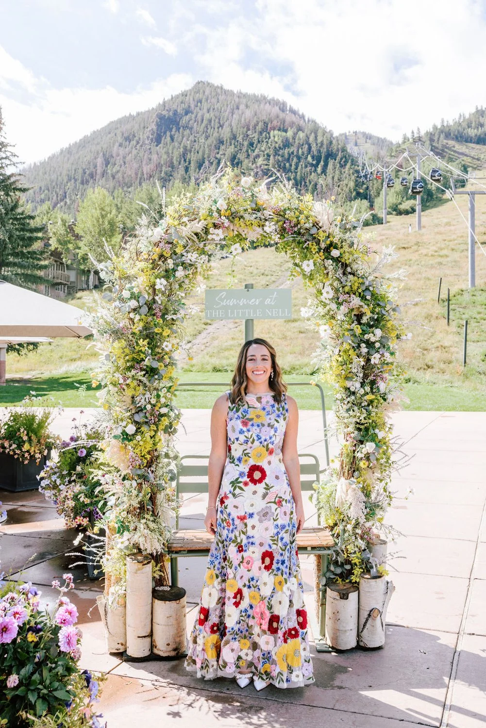 Bride standing under a the large wildflower arch at The Little Nell, Aspen, with mountains and gondola visible in the background.
