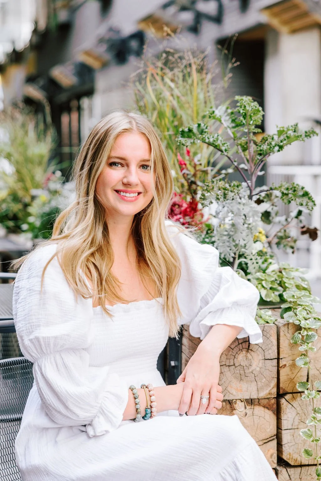 Denver headshot photographer Betsi Ewing smiling in a white top with greenery at Dairy Block