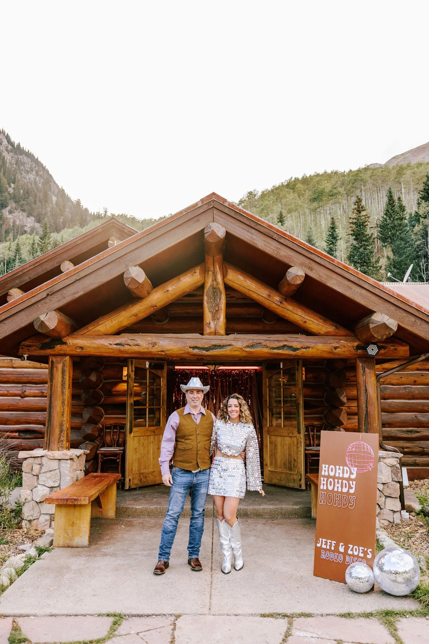 Couple in reception outfits in the doorway of Pine Creek Cookhouse with rodeo disco party signage and decorations, Aspen area Colorado mountain wedding