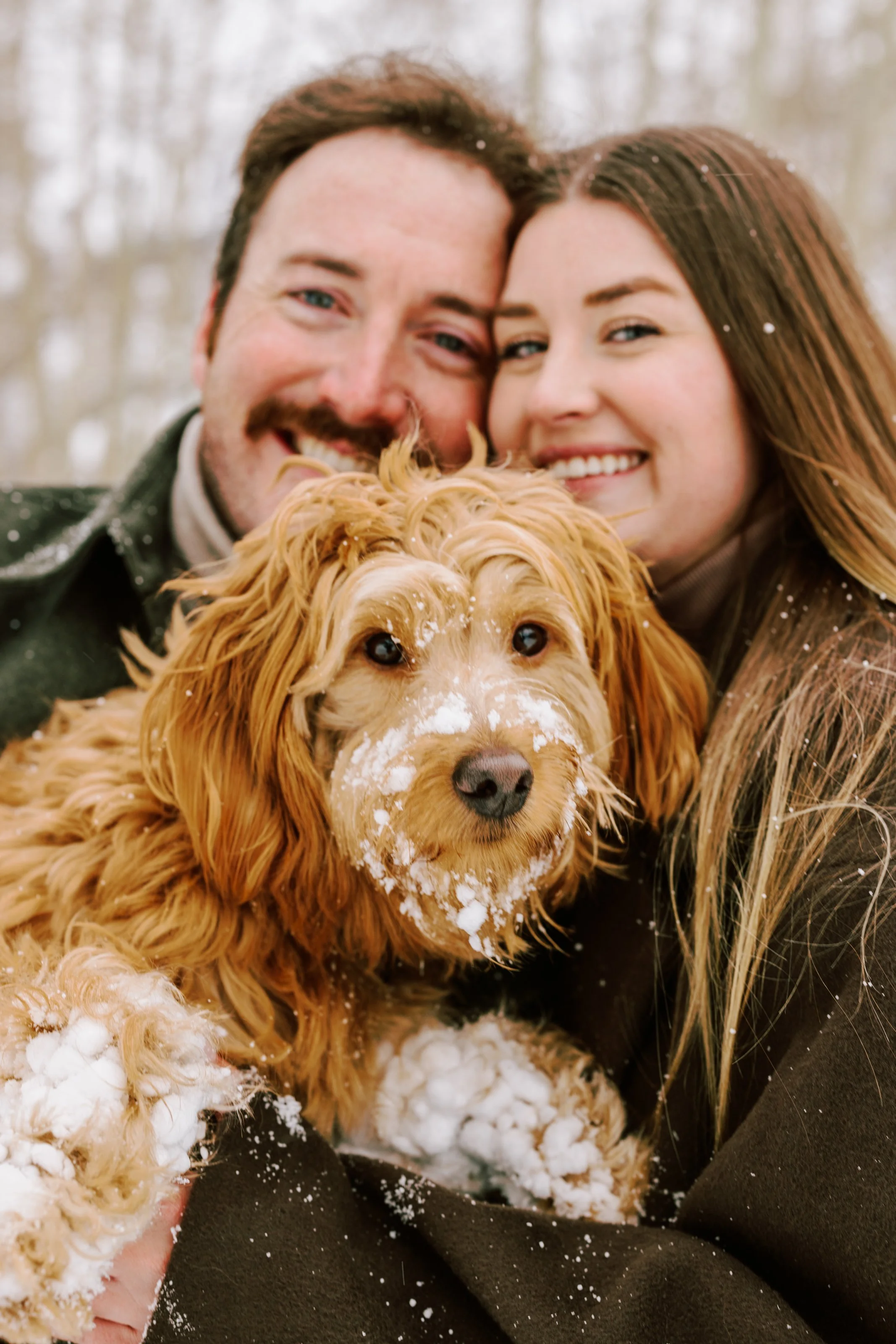happy couple smiling with their dog who is covered in snow during an engagement session in aspen, colorado