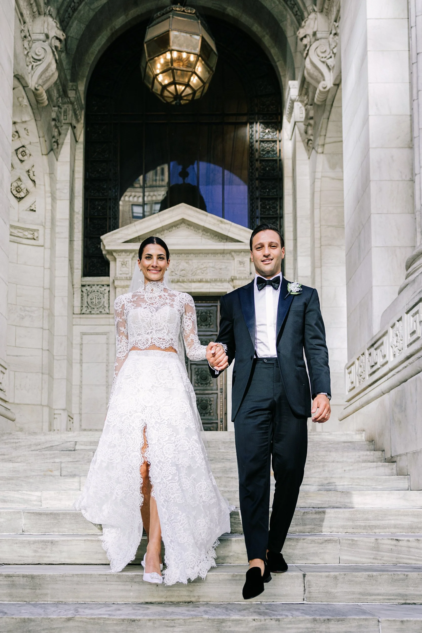 Bride and groom walking down the steps of the New York Public Library beneath the ornate lantern entrance, NYC wedding