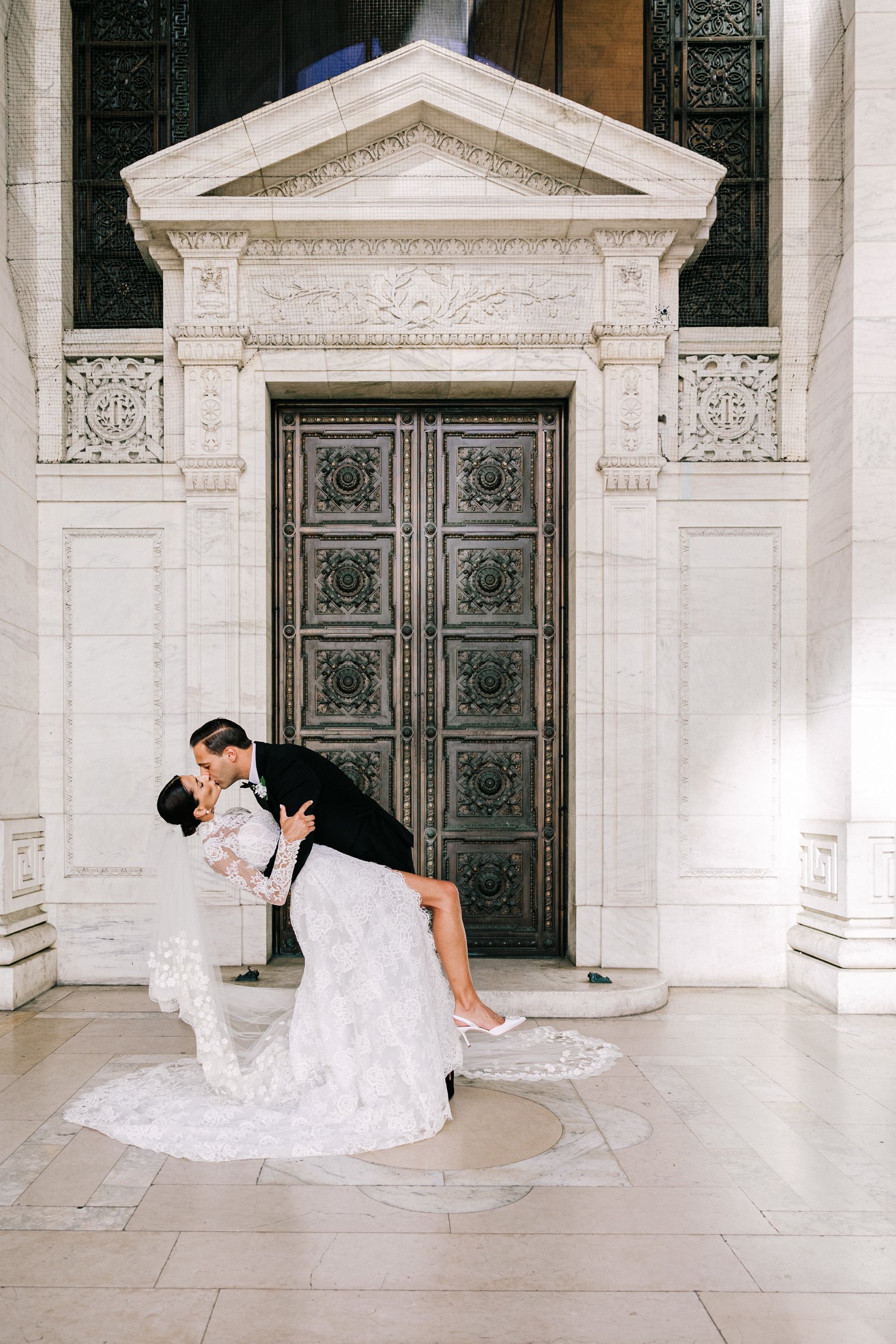 Bride and groom kissing on the exterior steps of the New York Public Library with the ornate columns and bronze doors behind them