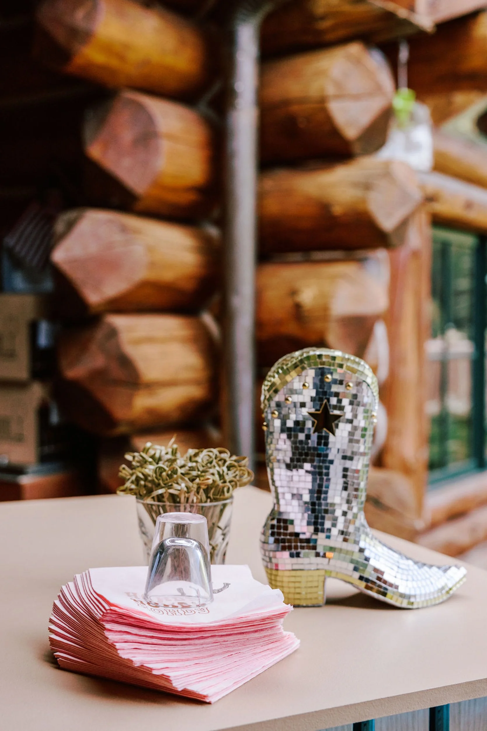 Cowboy boot used as a floral vase with greenery alongside a disco ball and pink napkins, creative table detail at Pine Creek Cookhouse rodeo disco wedding in Aspen Colorado